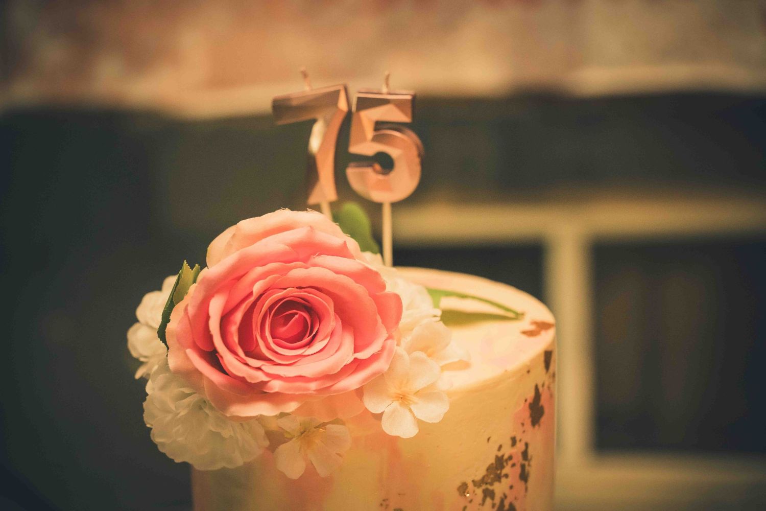 Close-up of a delicate pink and white birthday cake with fresh rose decorations.