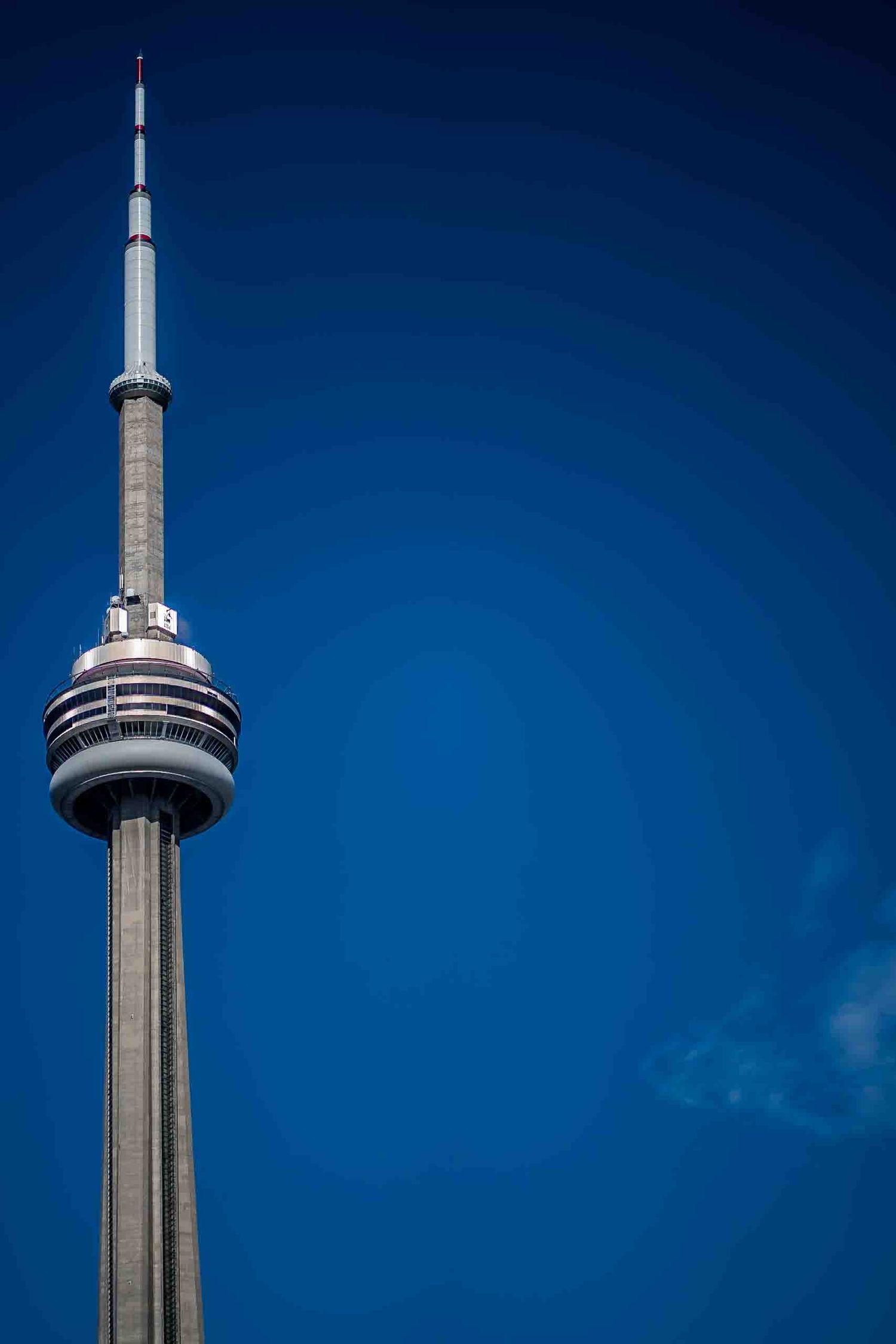 Toronto CN Tower rises against deep blue sky in dramatic architectural shot.