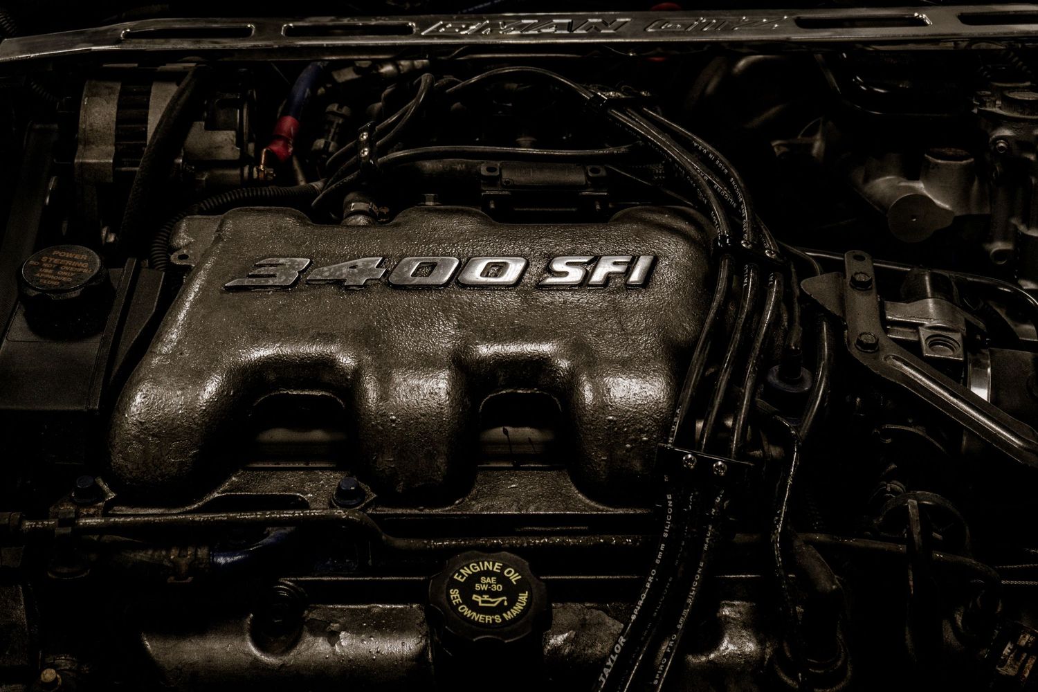 Close-up of a 3400 SFI engine in a car engine bay, showing detailed components and dark metallic surfaces.