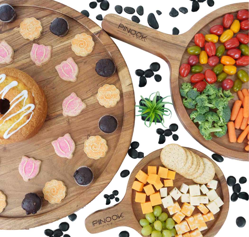 Pinook wooden charcuterie boards displayed with colorful snacks including vegetables, cheese, cookies, and fruit.