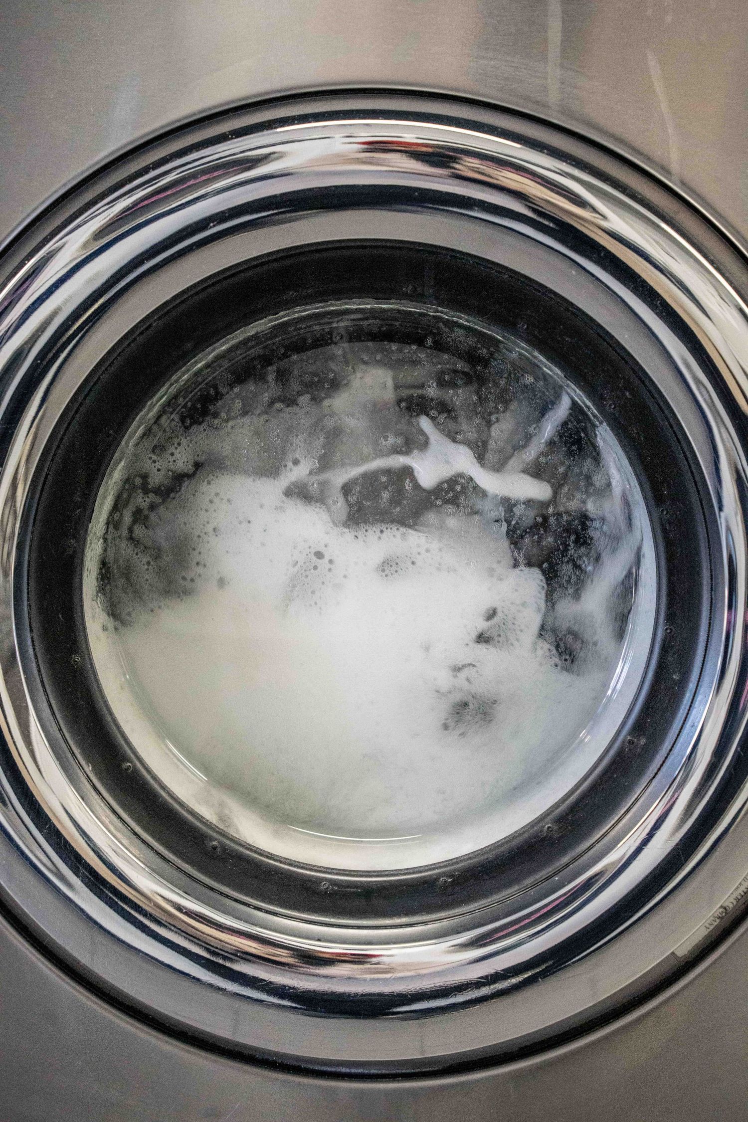 Close-up view of a washing machine drum filled with soapy white foam and water during a wash cycle.