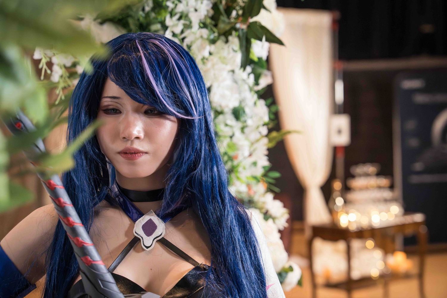 A cosplay photoshoot featuring a person with vibrant blue hair in an ornate indoor setting with floral decorations.