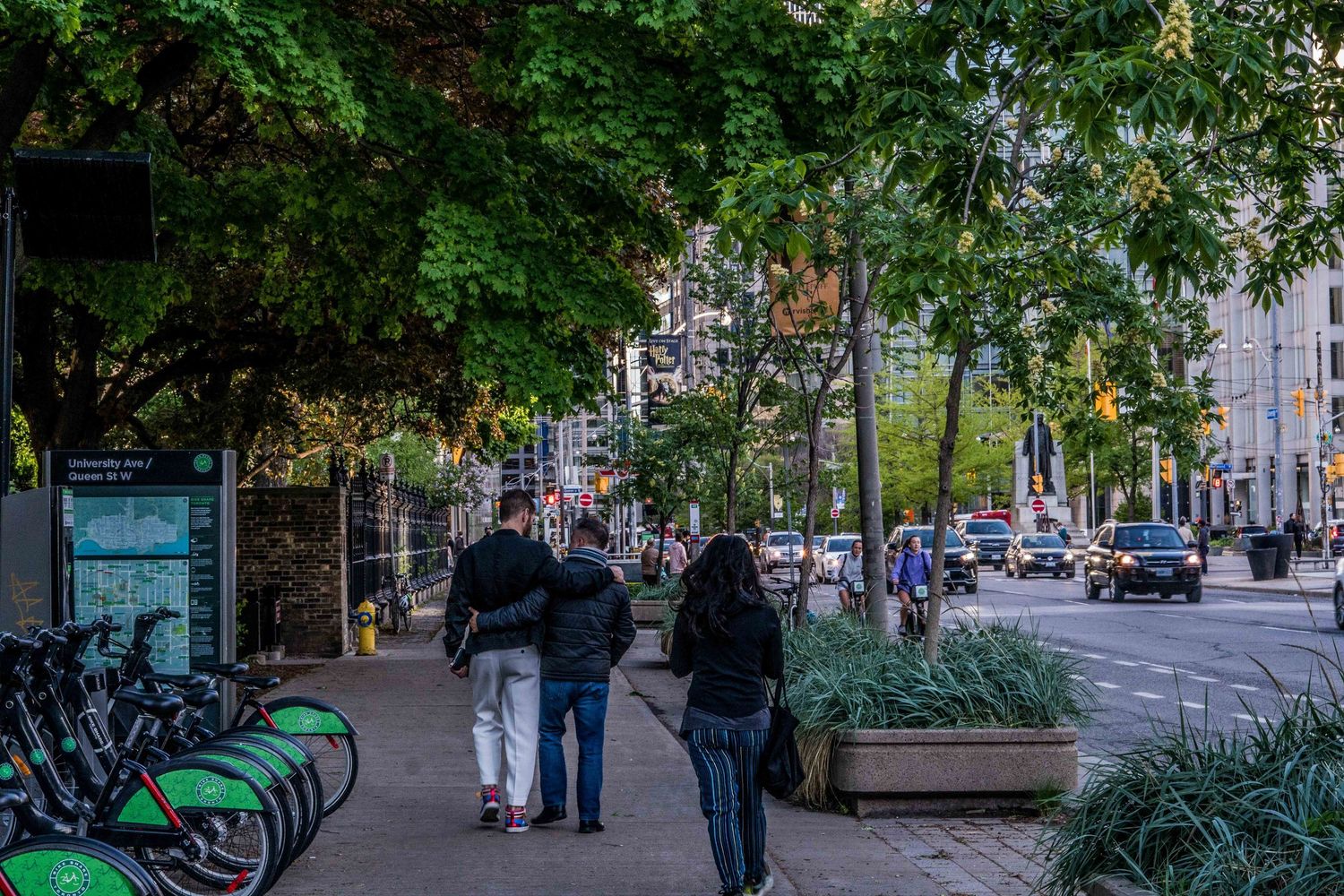Tree-lined urban street with benches and pedestrian walkways in a city setting.