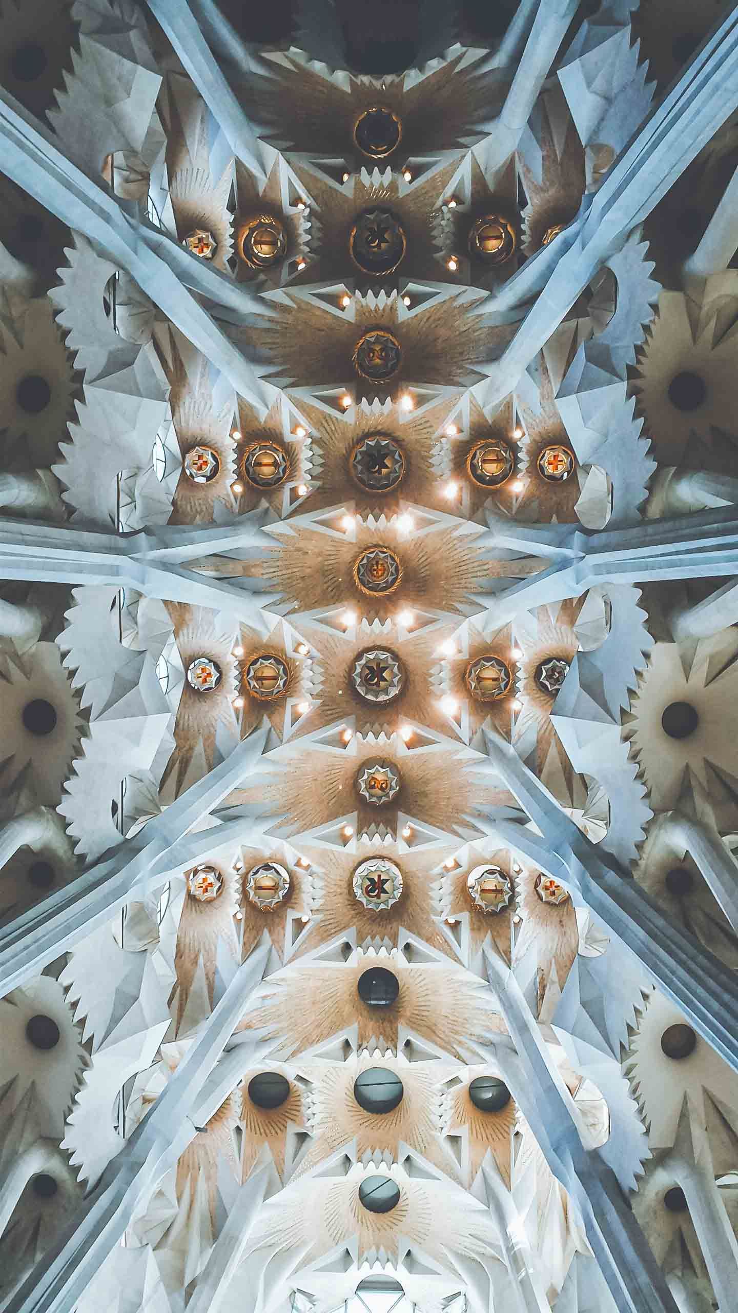 Ornate cathedral ceiling with intricate geometric patterns and golden light fixtures arranged in symmetrical rows.