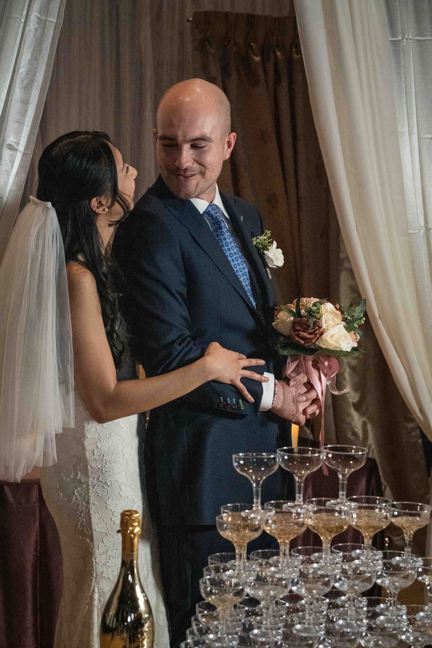 A couple shares an intimate moment at their wedding reception next to a champagne tower display.