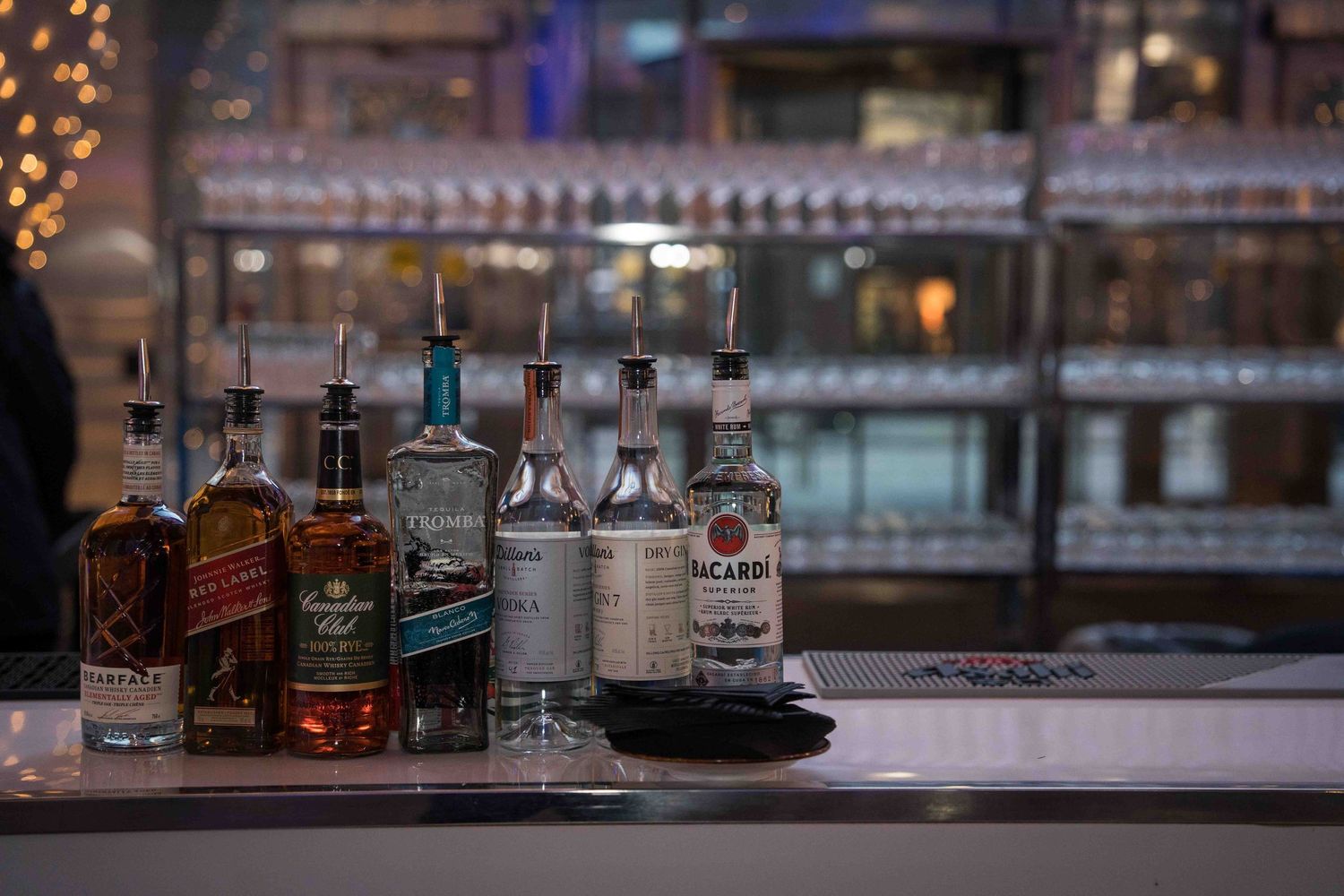 Bar counter with assorted liquor bottles and glassware in atmospheric evening lighting.