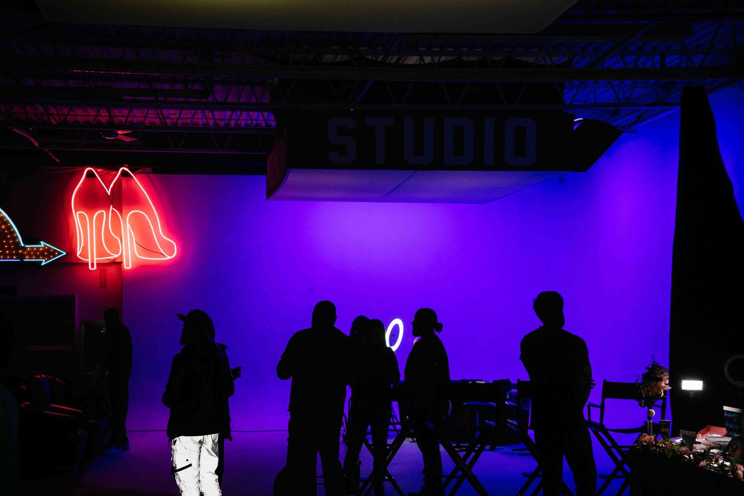 Silhouettes of people in a dark studio with neon lights and purple wall.