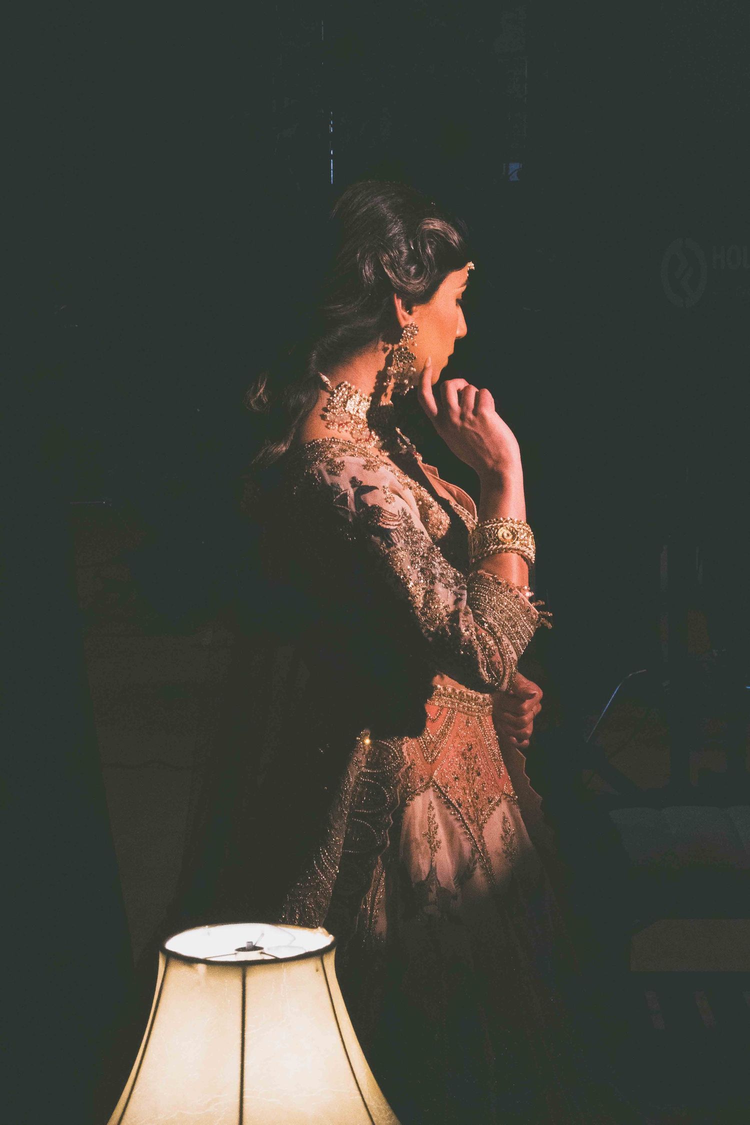 A silhouetted figure in an elegant lace dress stands in dramatic lighting next to a glowing table lamp.