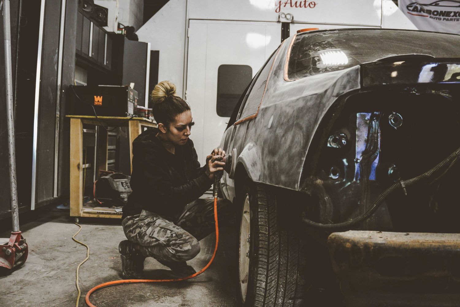 Person in black hoodie working on car detailing in an auto shop.