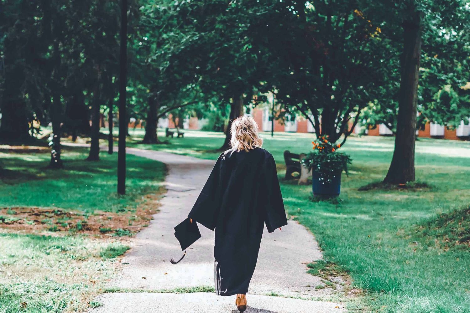 Person walking down a tree-lined pathway in a verdant park setting.