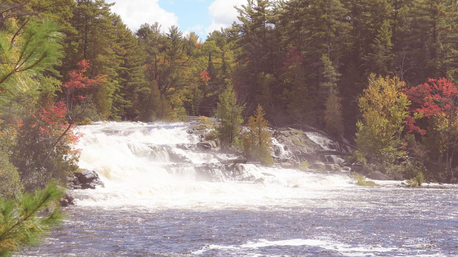 Rushing white water rapids flowing through a rocky river gorge lined with colorful fall foliage.