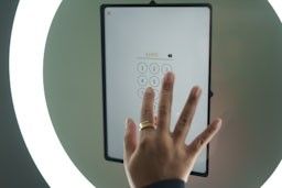 Hand interacting with a tablet device mounted on a wall showing a numeric keypad interface.