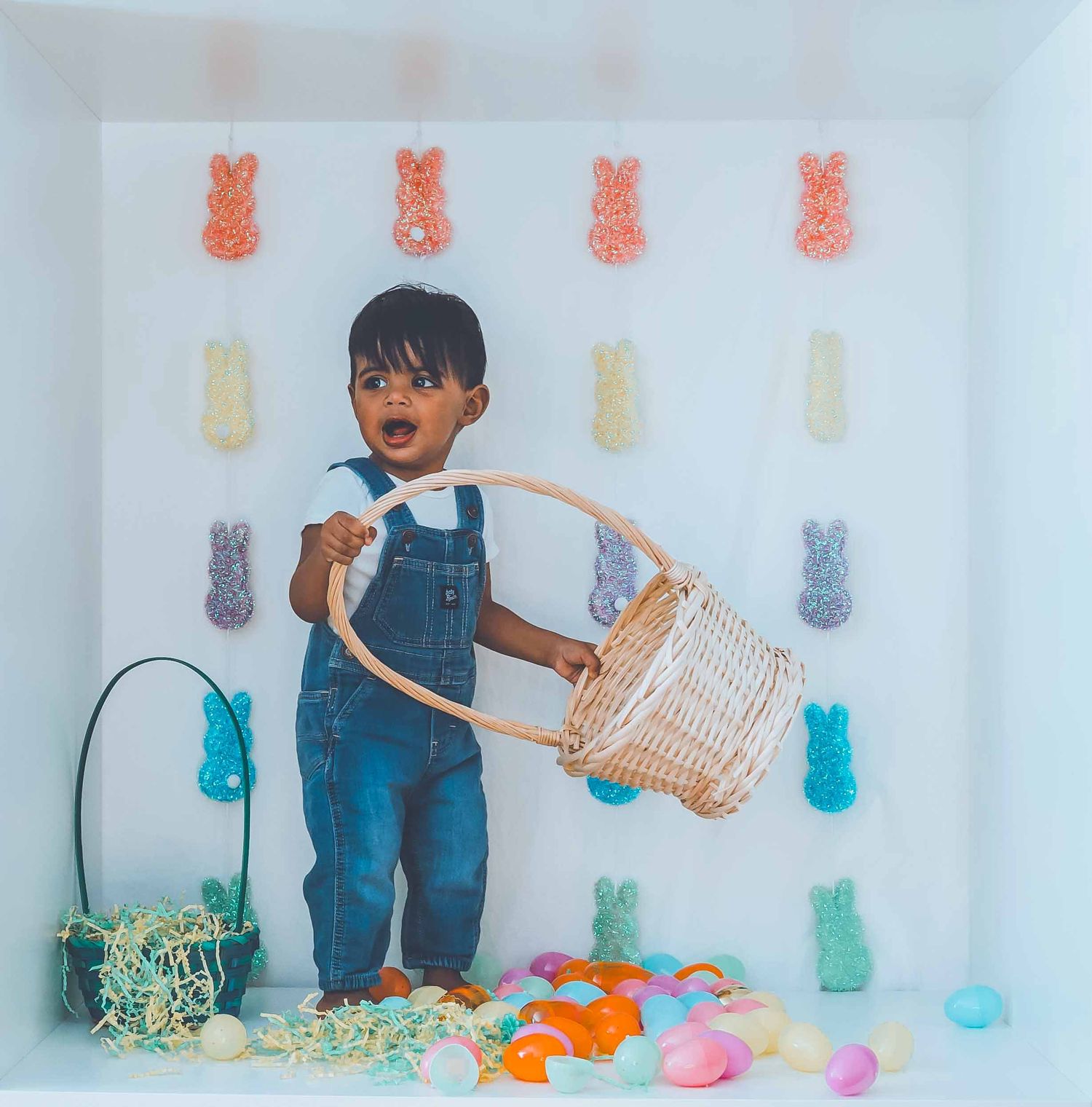 Easter themed photo shoot with colorful eggs and decorations against white backdrop.