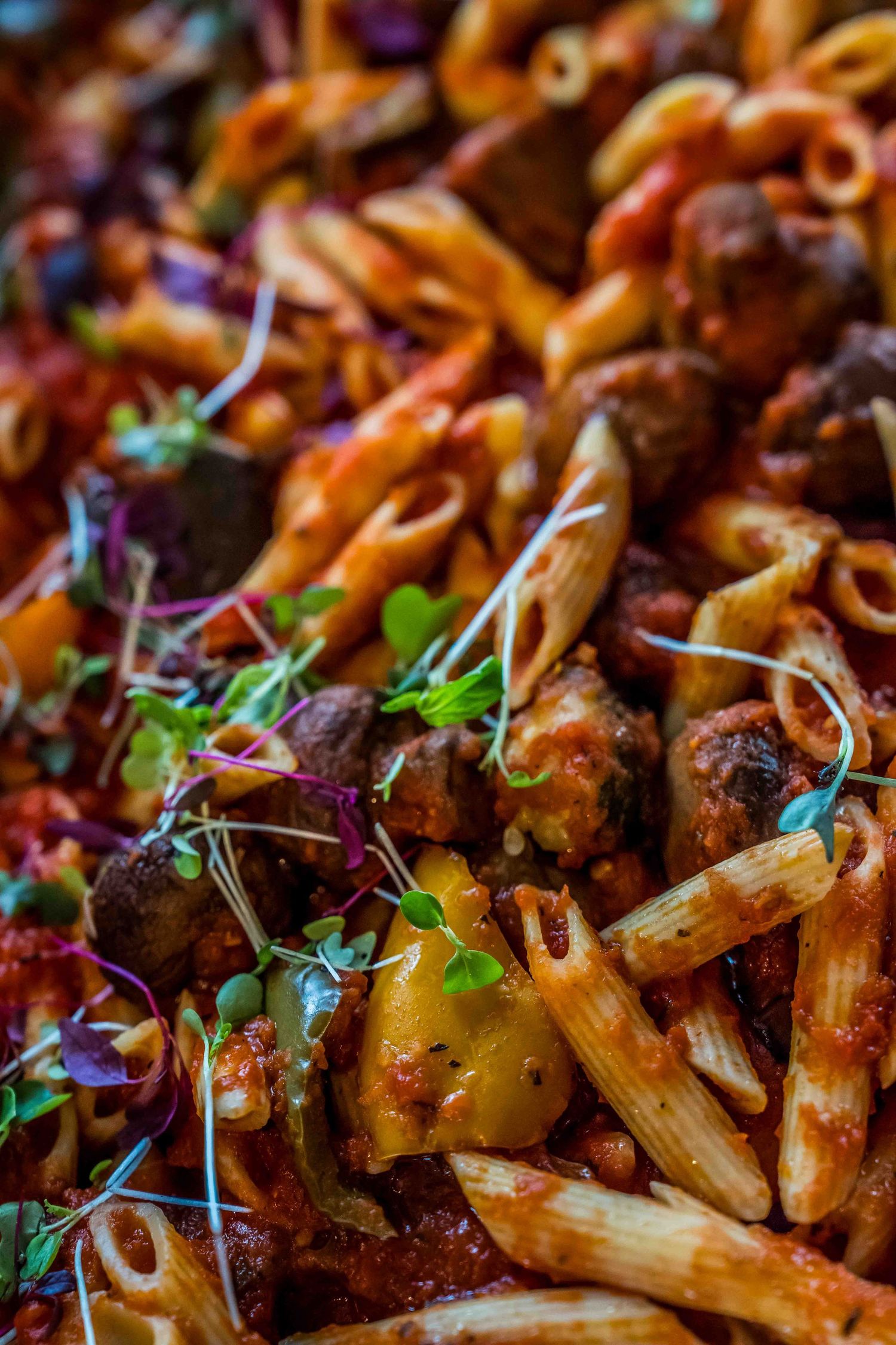 Close-up of penne pasta with meatballs in tomato sauce garnished with fresh microgreens herbs.