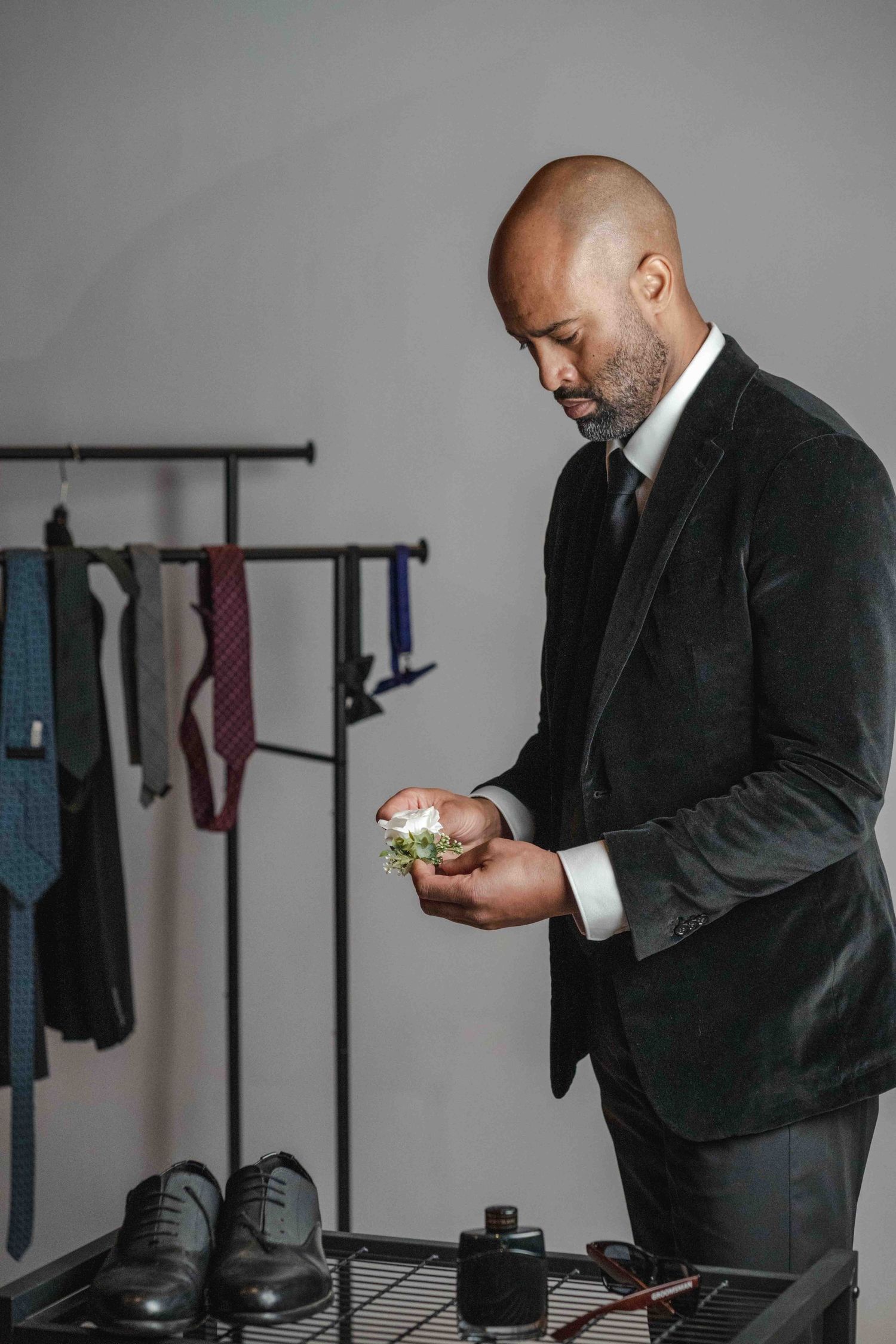 Professional in dark suit checking phone while standing near coat rack in minimalist office setting.