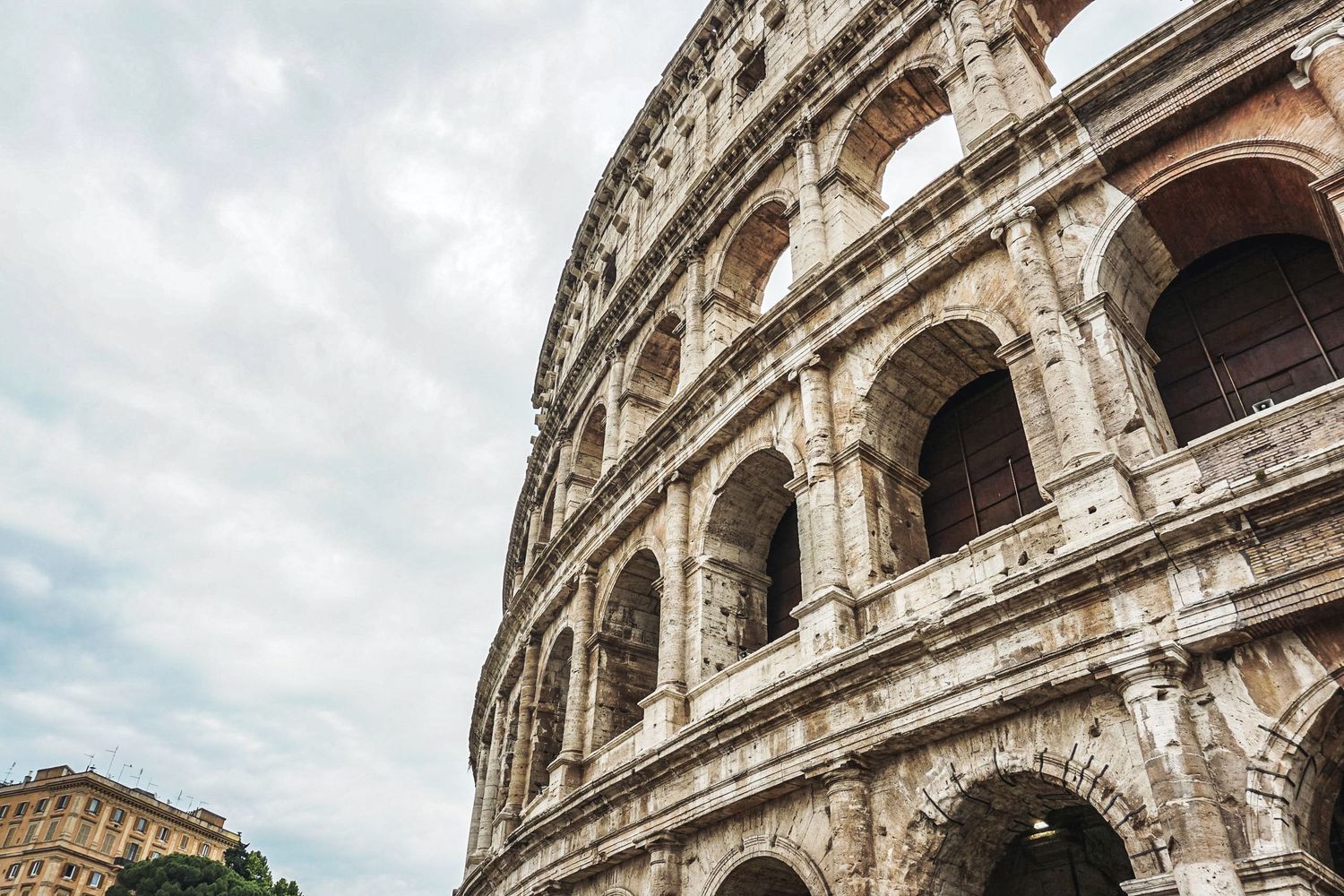 Ancient Roman Colosseum exterior with dramatic cloudy sky and stone arches in Italy.