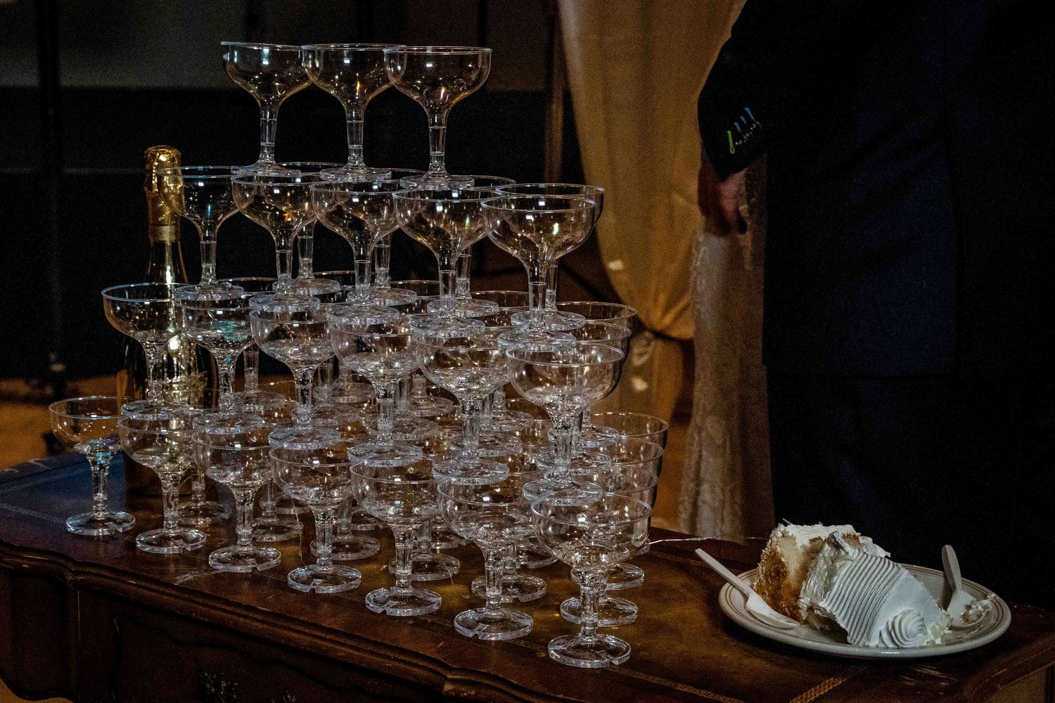 A pyramid of empty champagne glasses stacked elegantly on a dark wooden table with a plate in the background.