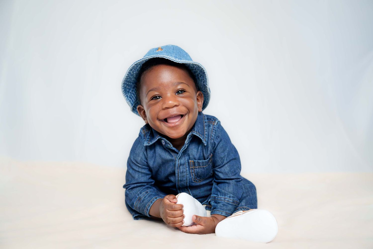 Smiling toddler in denim jacket and cap posing for series of portraits.