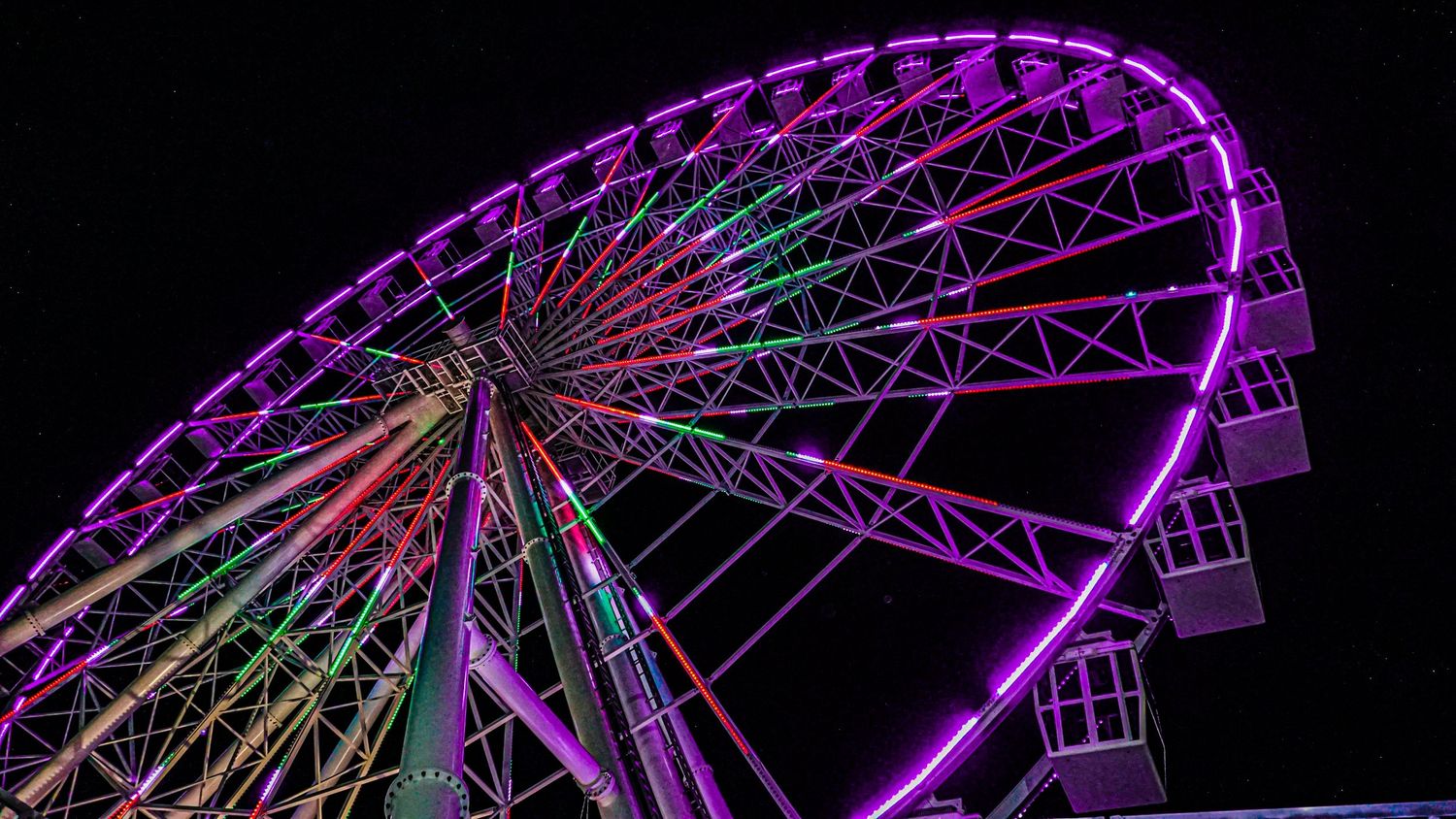 Illuminated Ferris wheel glowing in purple and green against night sky.