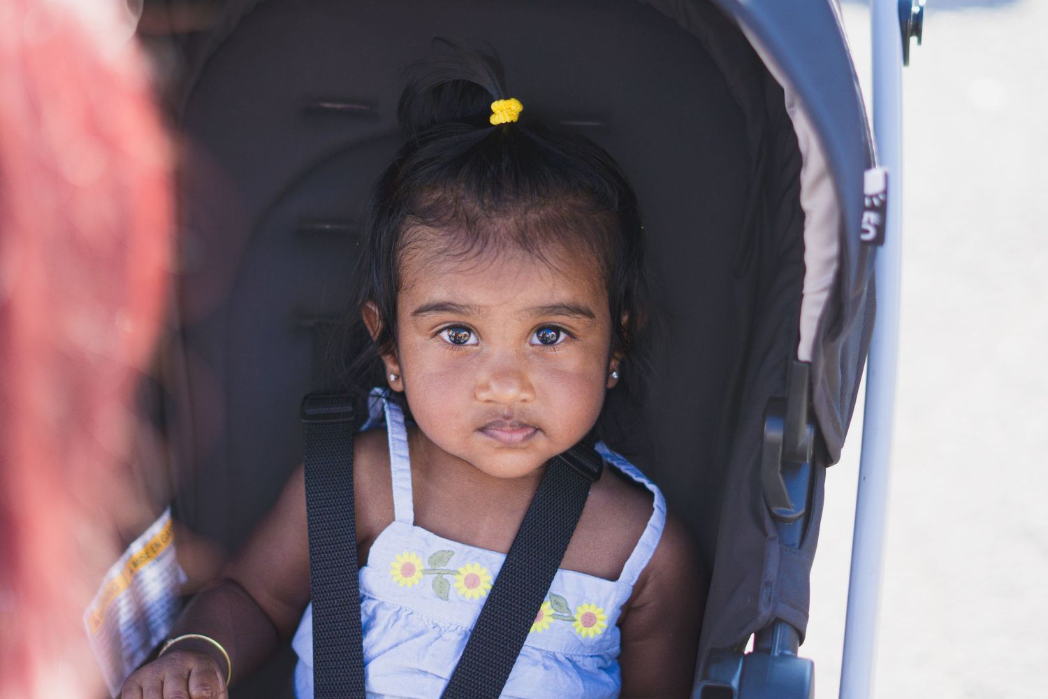Row of young children seated in black car seats or strollers.