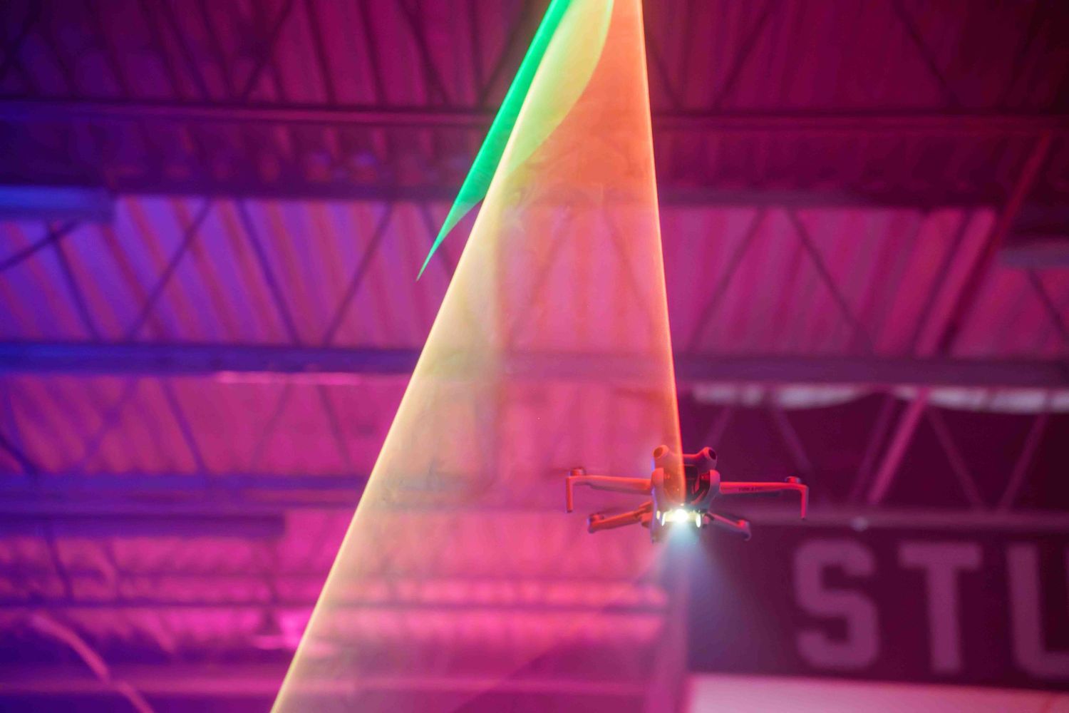 A drone navigates through dramatic laser light beams in a pink-lit studio environment.