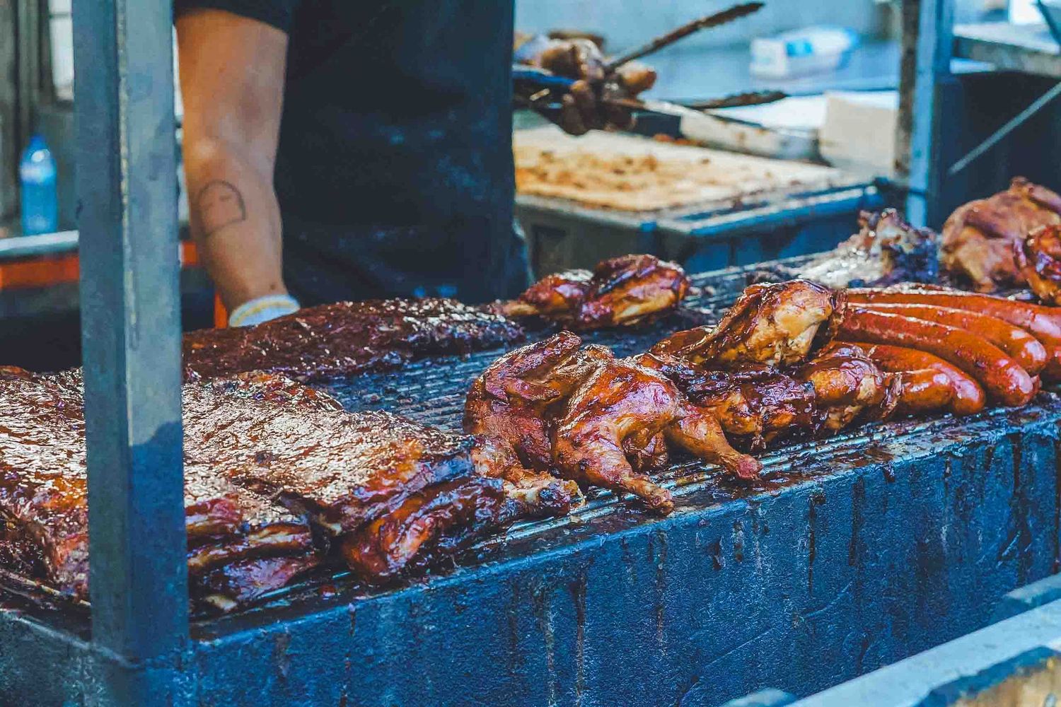 Grilled meats on a blue cooking surface with smoke rising.