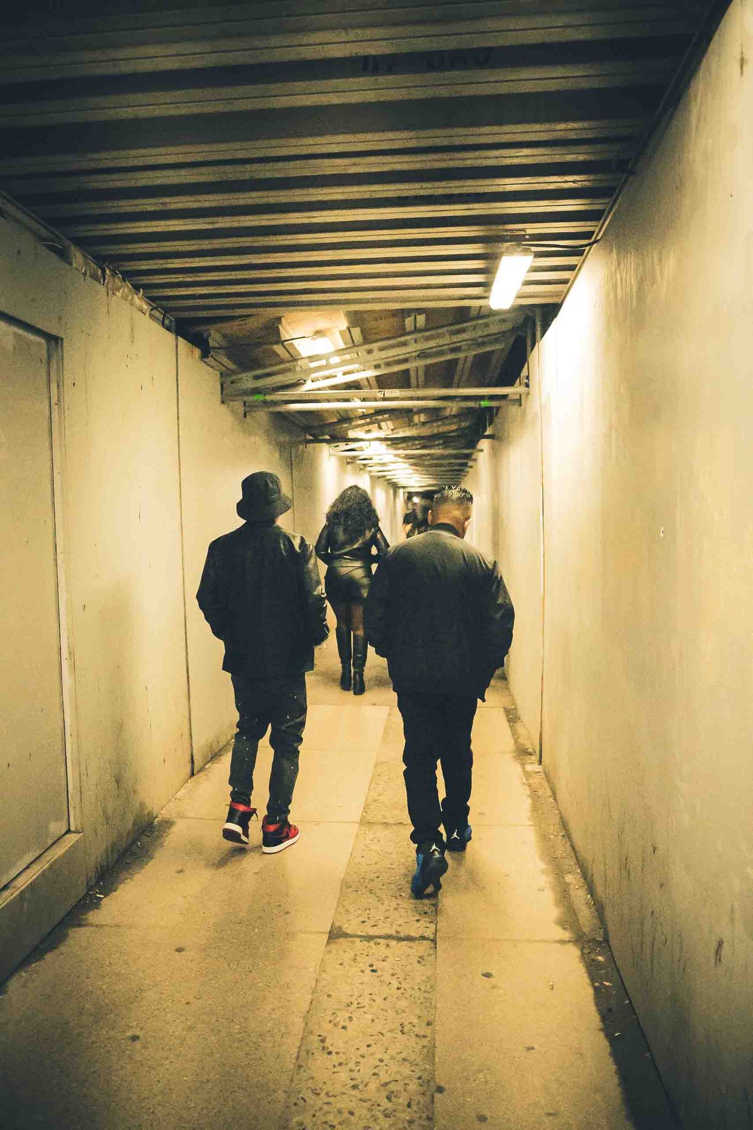 People walking through a dimly lit underground tunnel or passageway.