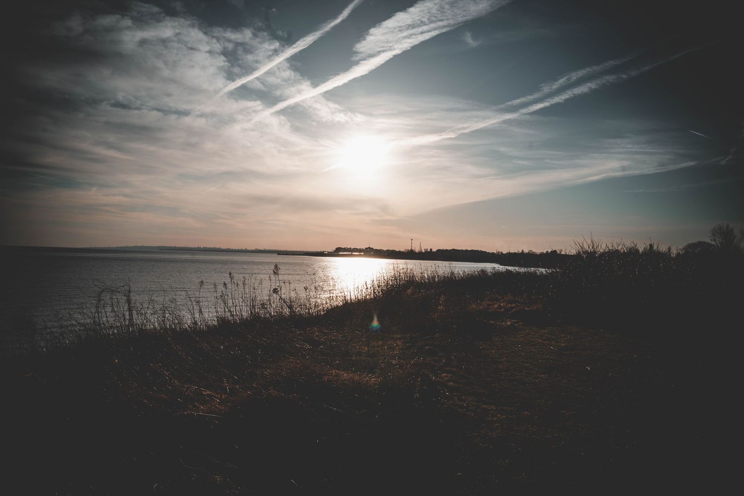 Dramatic panoramic sunset landscape with contrails streaking across a cloudy sky.