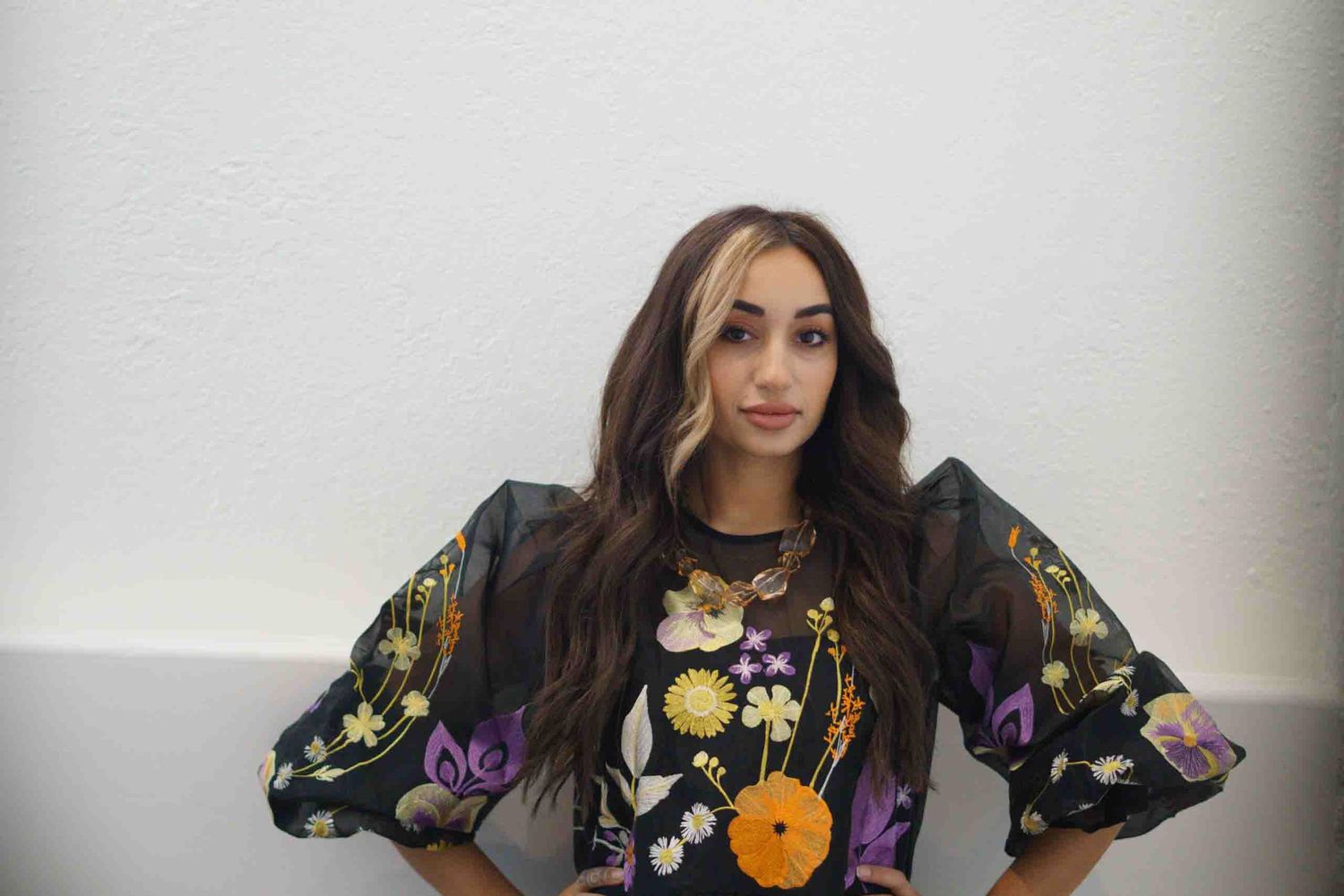 Fashion photography session featuring dark floral dress against white studio walls.