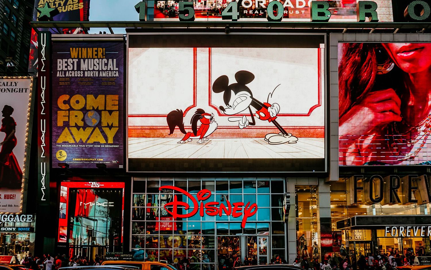 Broadway theater district panorama showing colorful illuminated marquees and billboards at night.