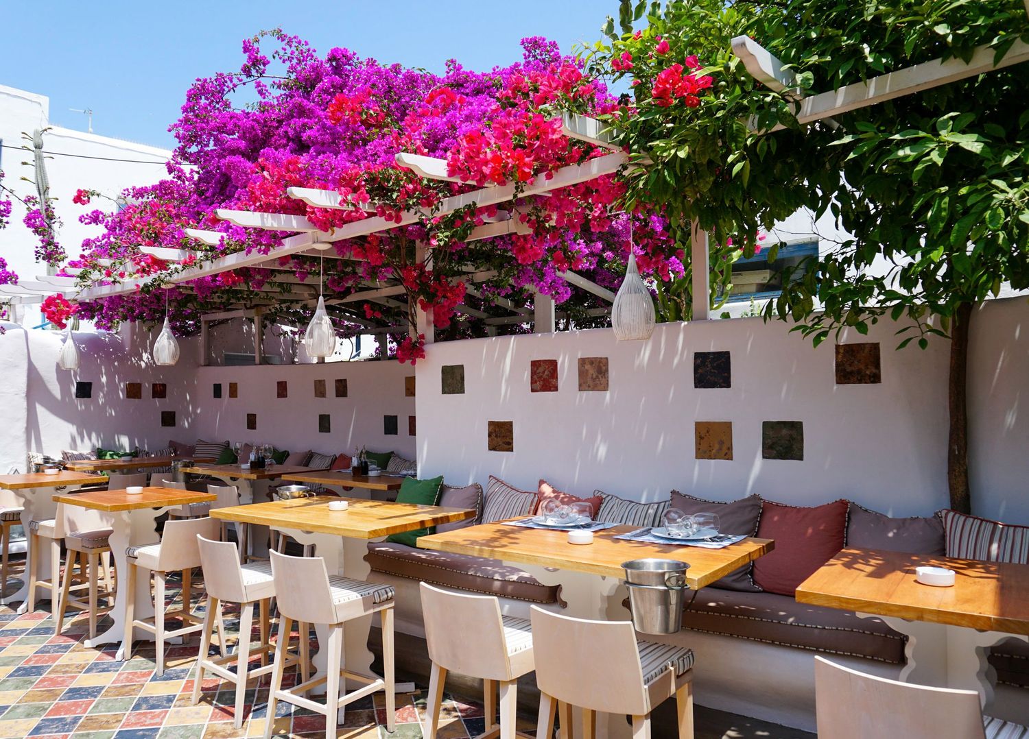 Outdoor dining terrace with purple bougainvillea covered pergola and white tables.