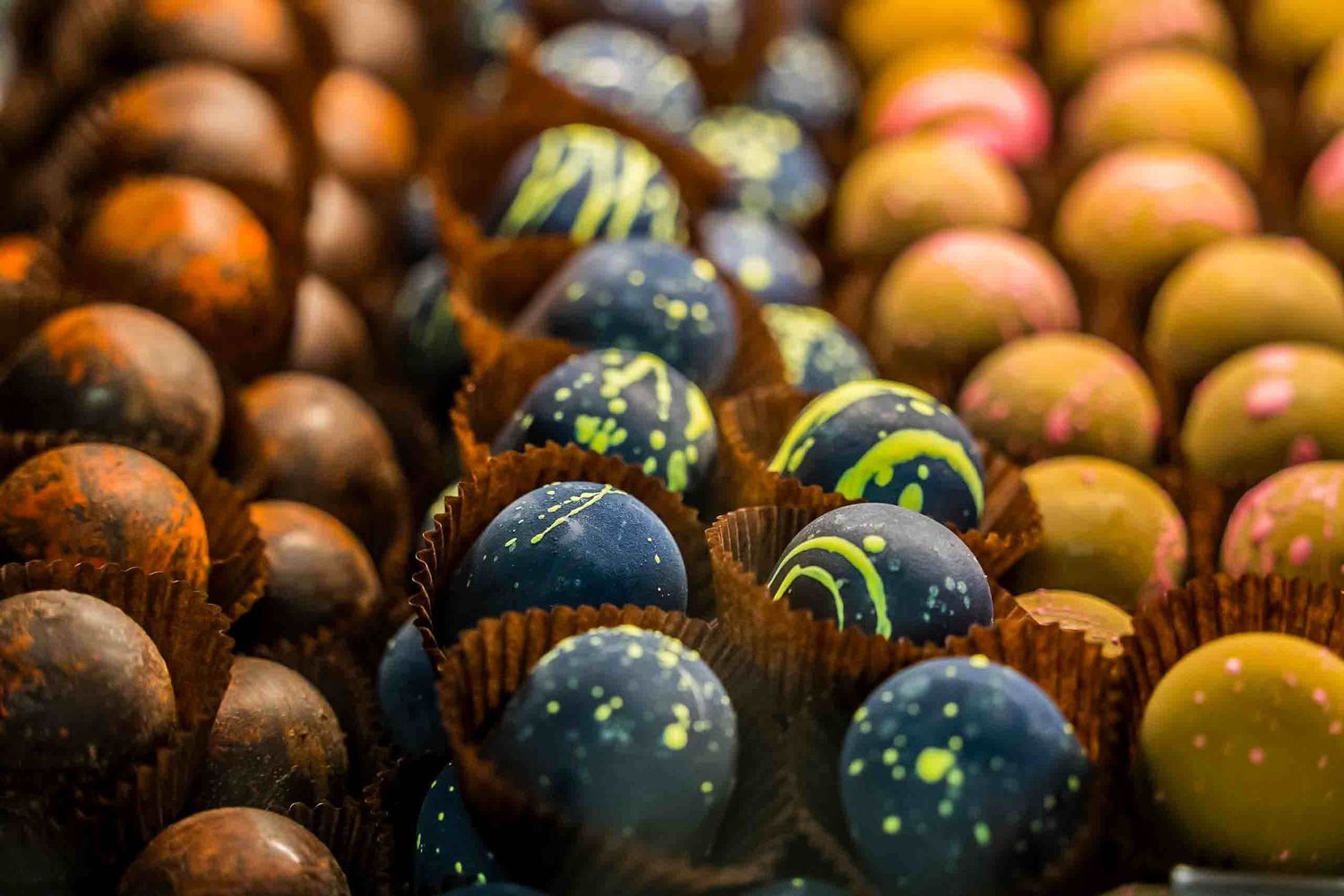 Artisanal chocolate truffles with colorful decorative toppings arranged in rows.