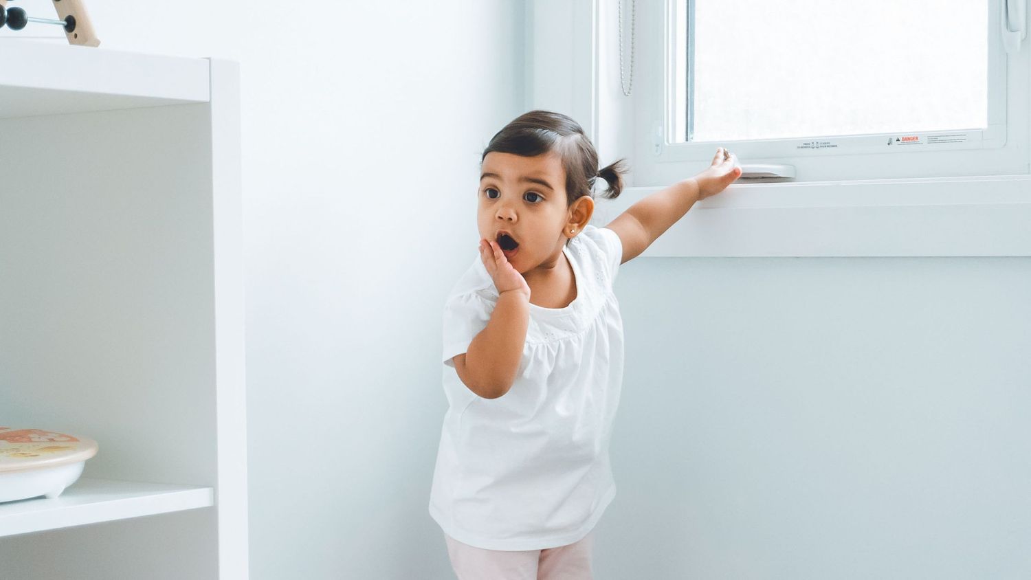 Young child in white shirt making dramatic pose against white wall.