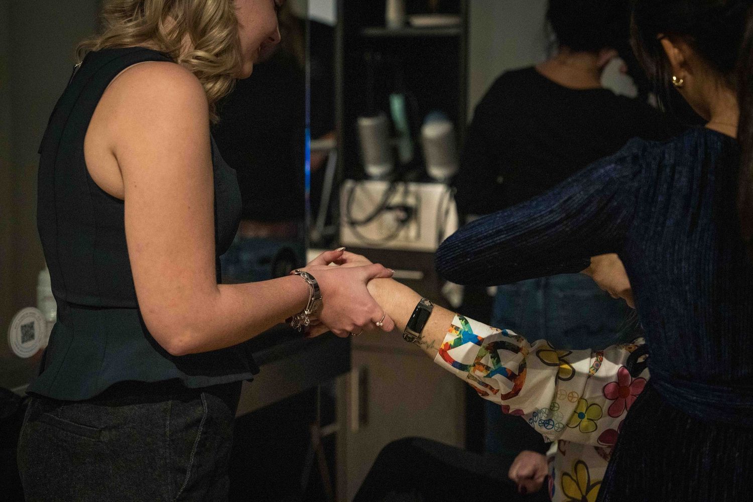Two women shaking hands in a dimly lit room, one wearing a floral patterned sleeve.