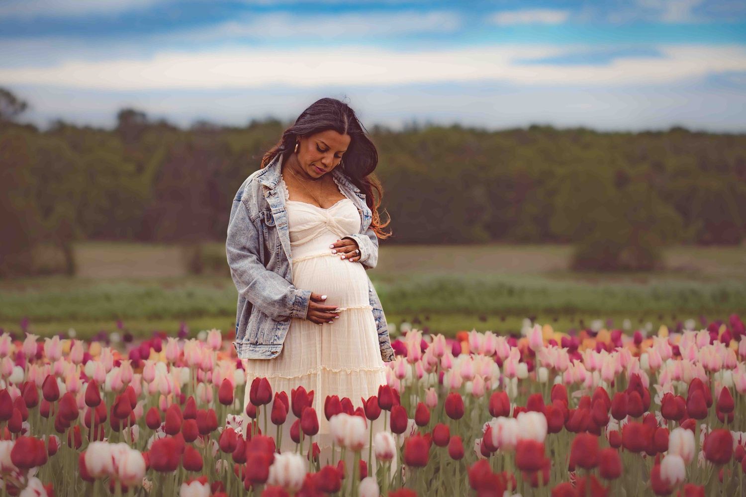 Maternity photo in dreamy light captures moment among pink and red tulips.