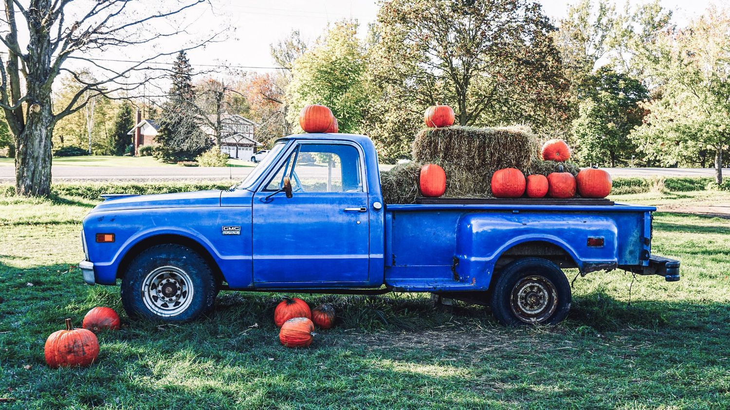 Vintage blue pickup truck filled with pumpkins and hay bales in an autumn farm setting.