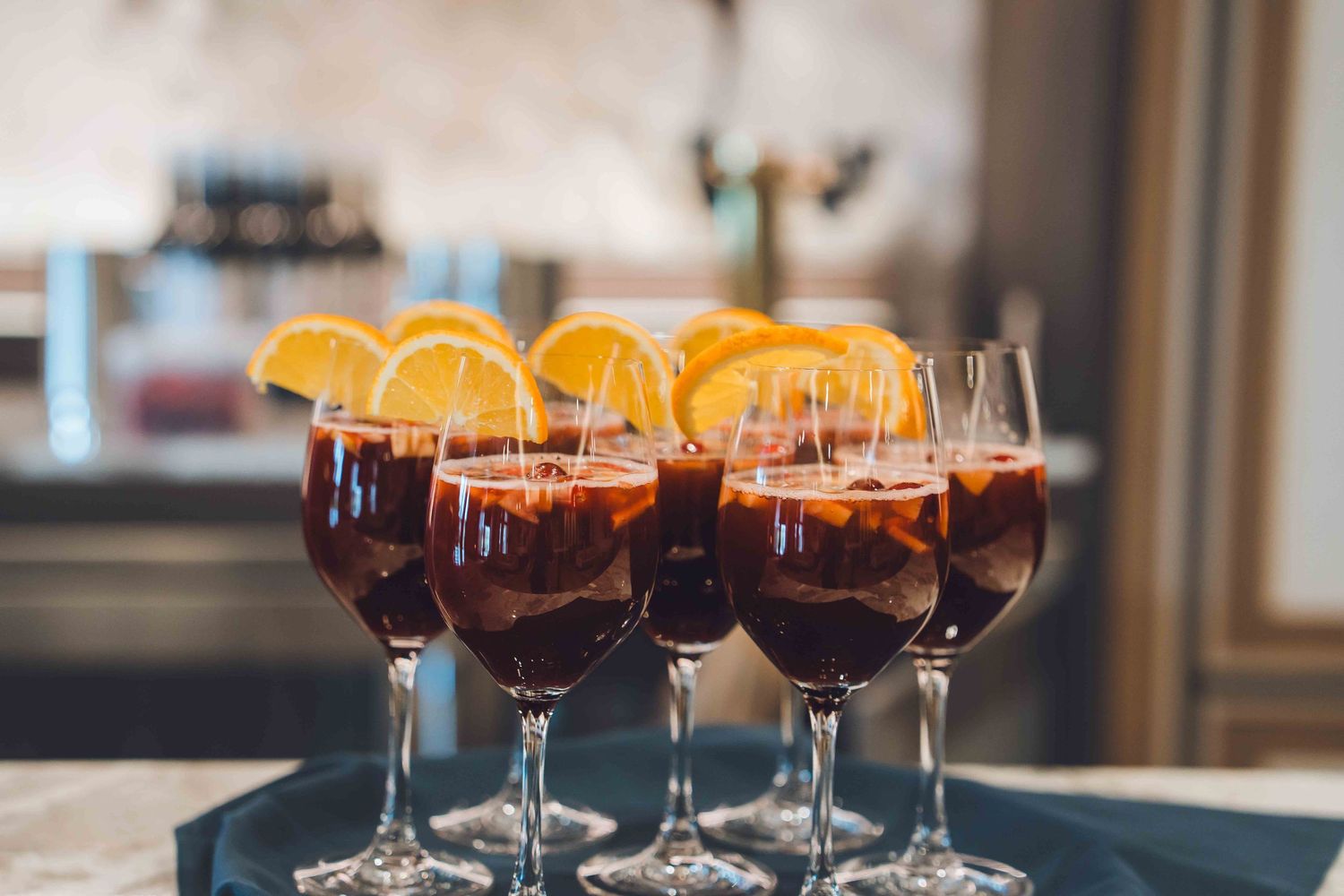 Elegant wine glasses filled with dark sangria cocktails garnished with fresh orange slices on a serving tray.