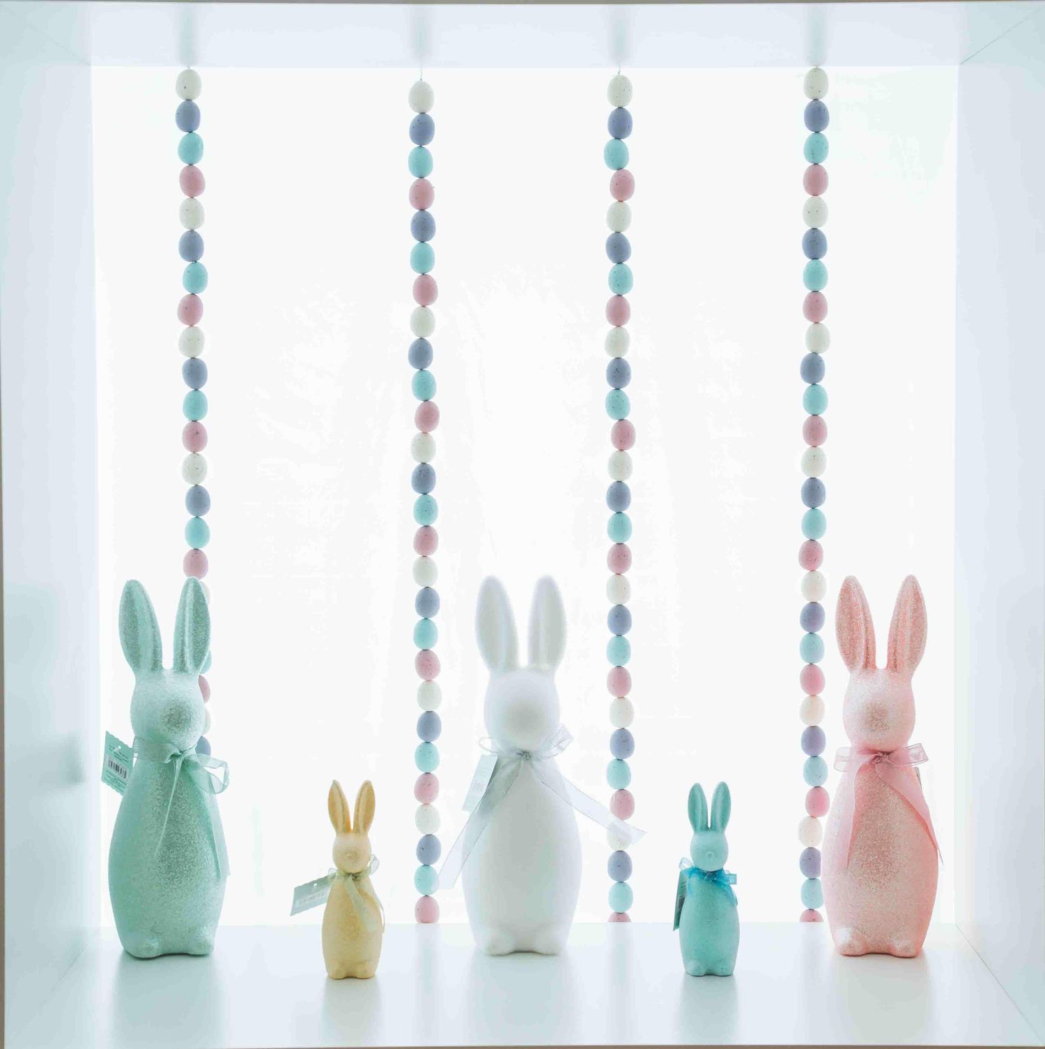 Row of decorative pastel bunny figurines with hanging blue and pink beaded garlands.
