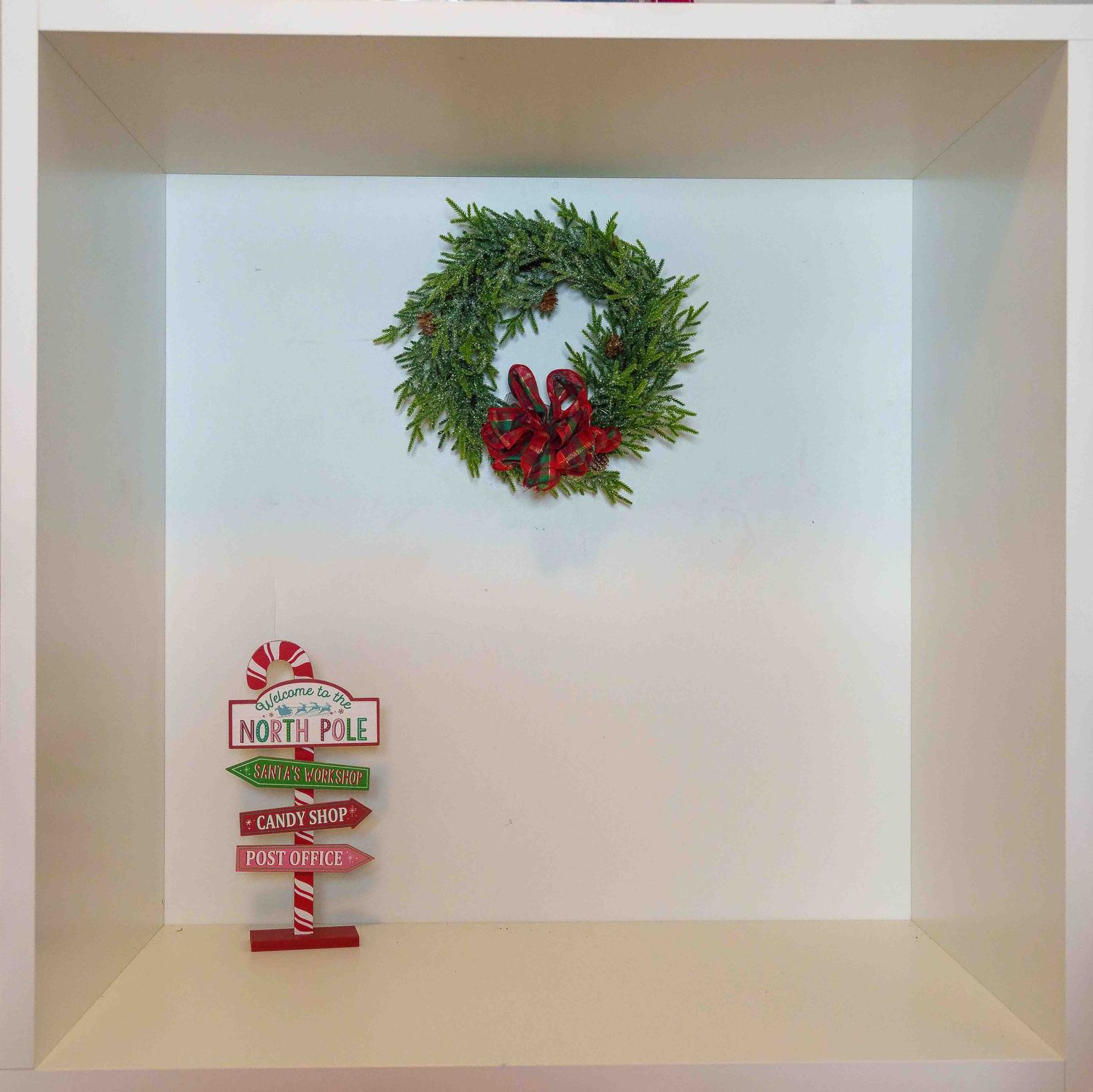 Empty white display shelf with holiday decorations and North Pole signage.