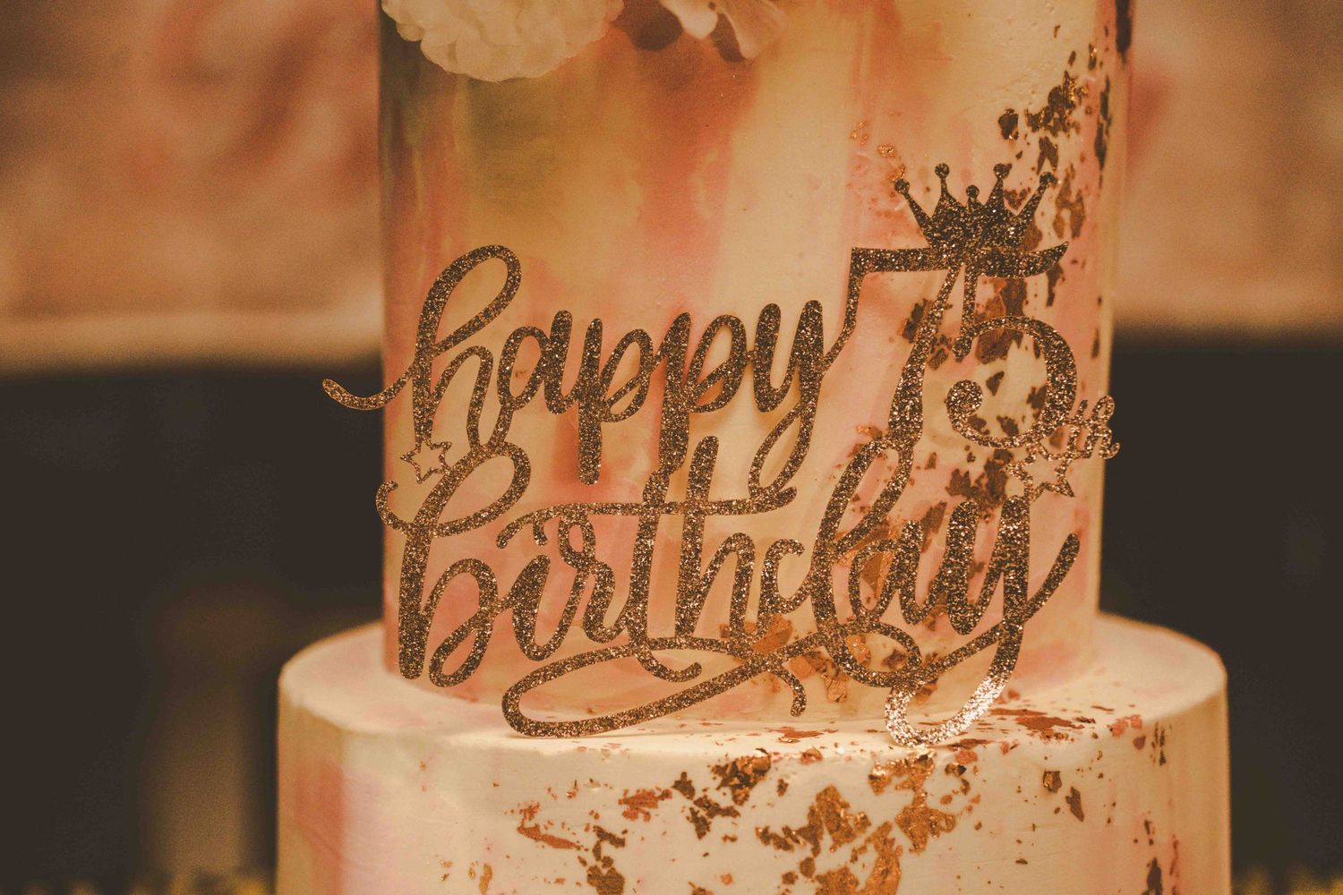 Birthday cake with gold lettering and pink floral accents on display.