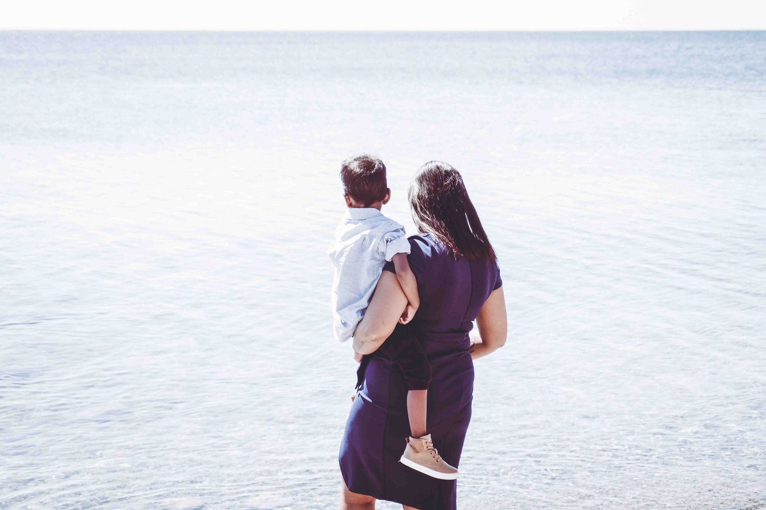 Couple walking along shoreline with bright blue water in background.