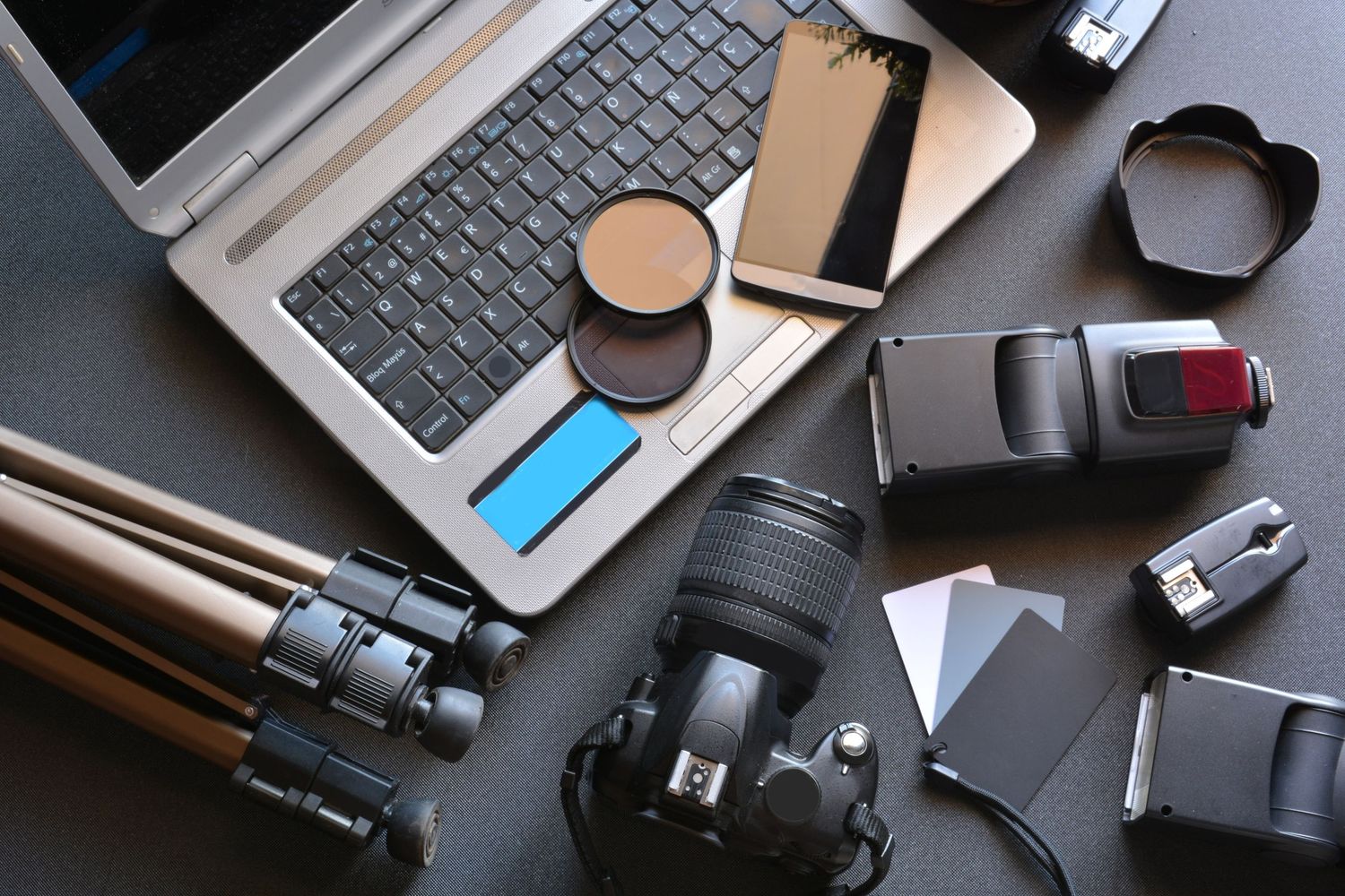 Flat lay of photography equipment including laptop, camera, and accessories on dark surface.