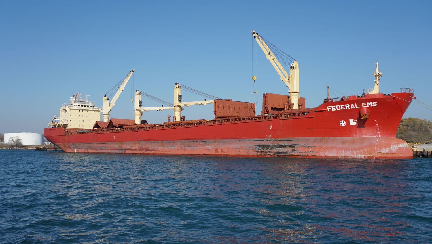 Red cargo ships sailing across blue ocean waters under clear skies.