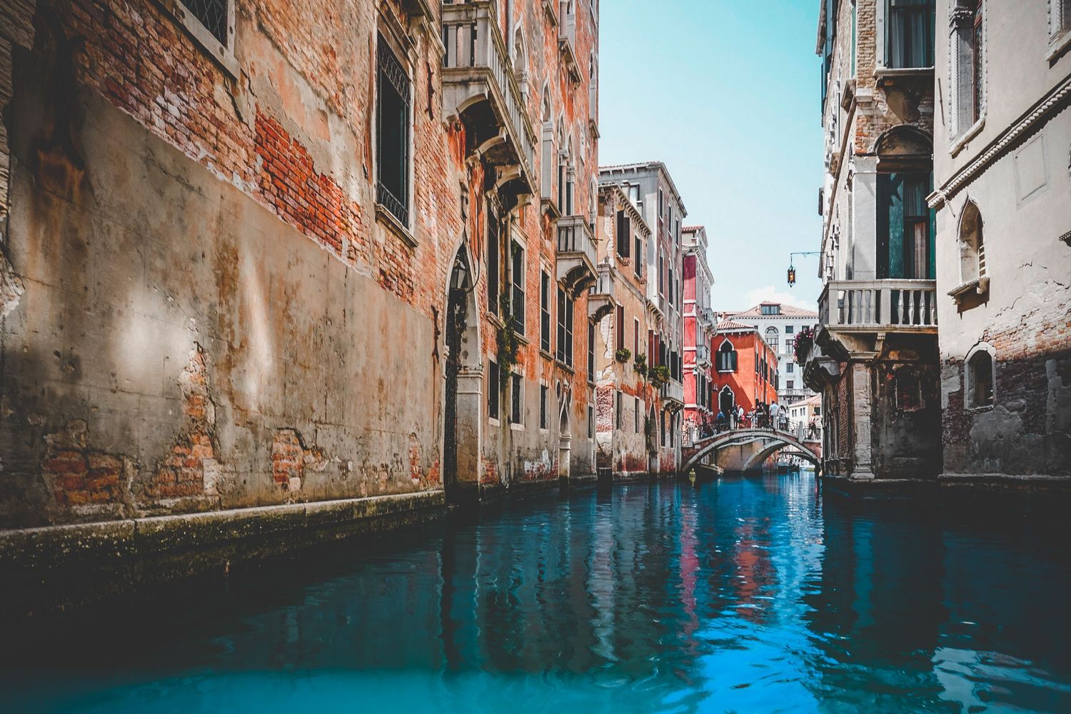 Narrow Venetian canal with reflective blue water between historic brick buildings and architecture.