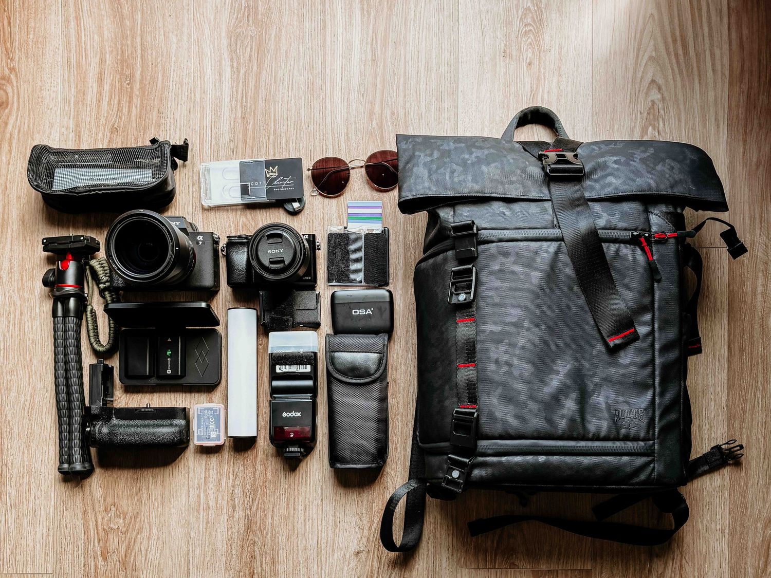 Professional photography gear including camera, lenses, flash and backpack laid out on wooden floor.