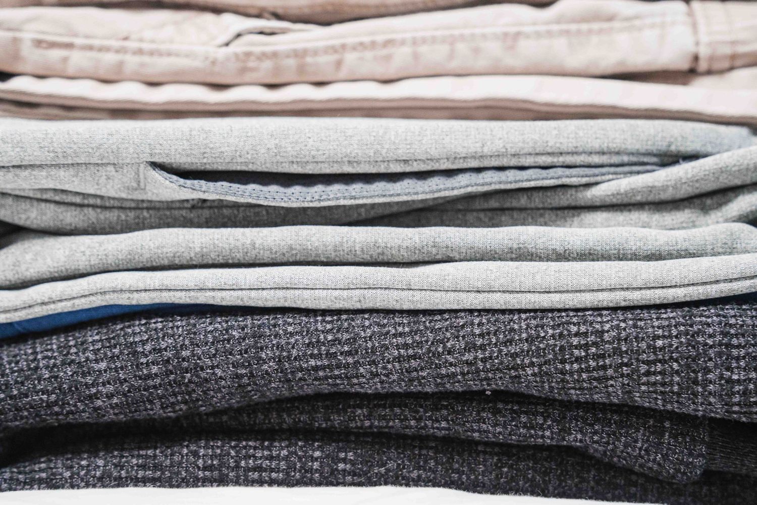 A neatly folded stack of gray and neutral-toned knit sweaters and pants arranged in a tidy pile.