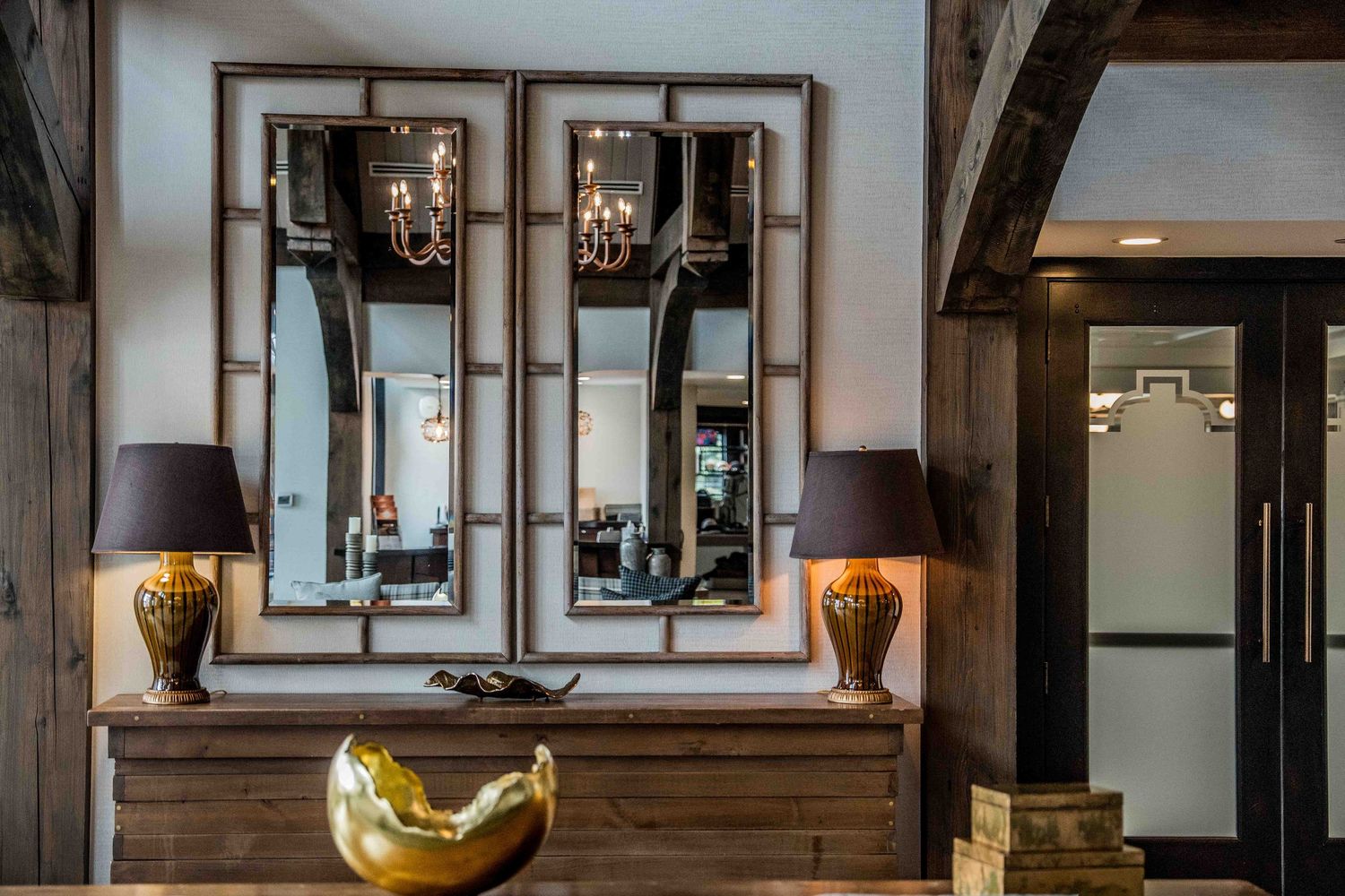 Elegant console table with gold lamps, decorative bowl, and ornate mirrors in a rustic luxury interior.