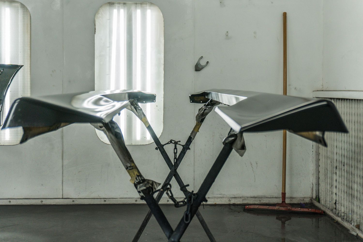 Two carbon fiber aerodynamic wings mounted on a metal stand inside an industrial workshop or paint booth.