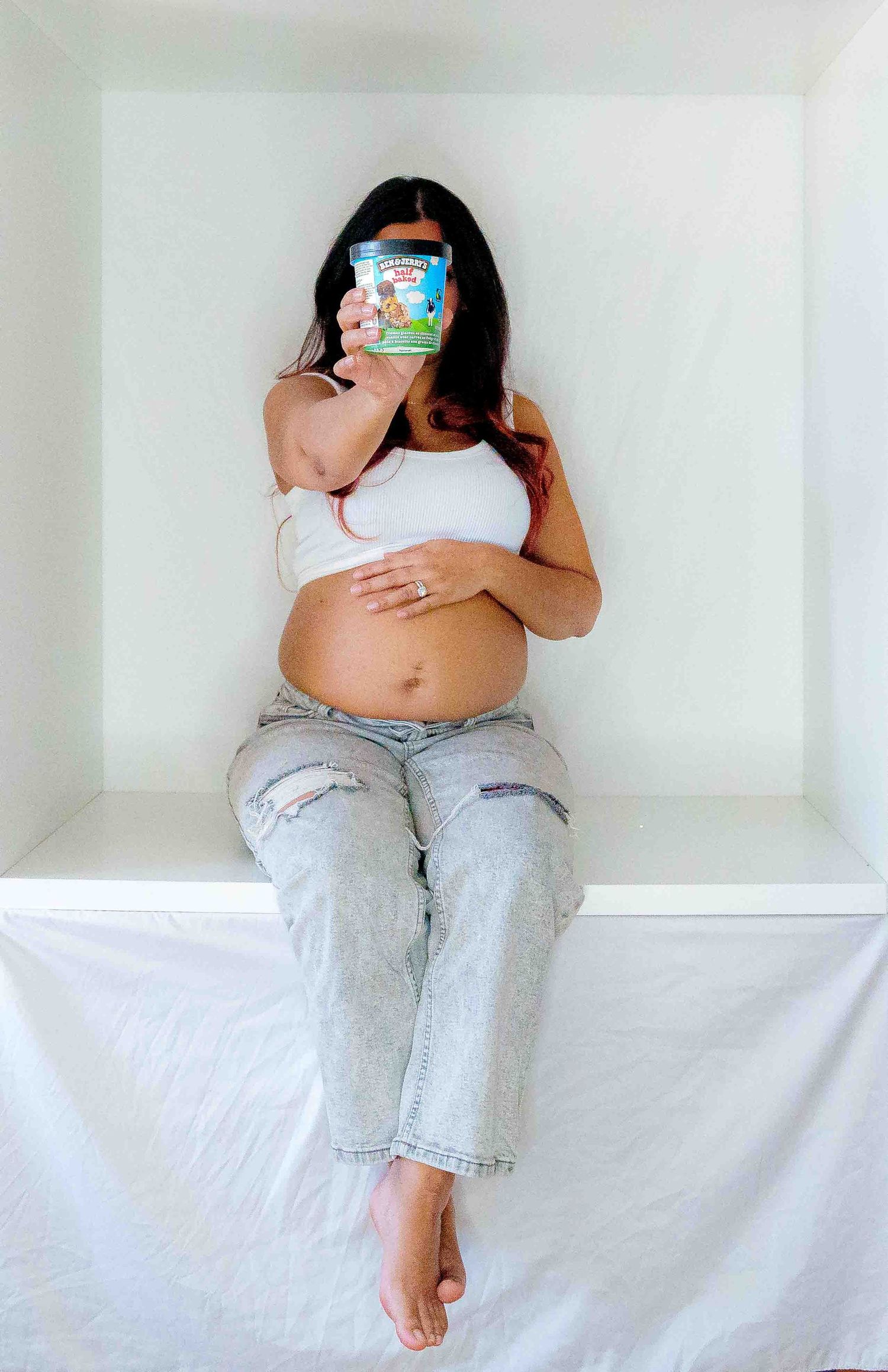 Maternity photo with Pokemon-themed prop in minimalist white setting.