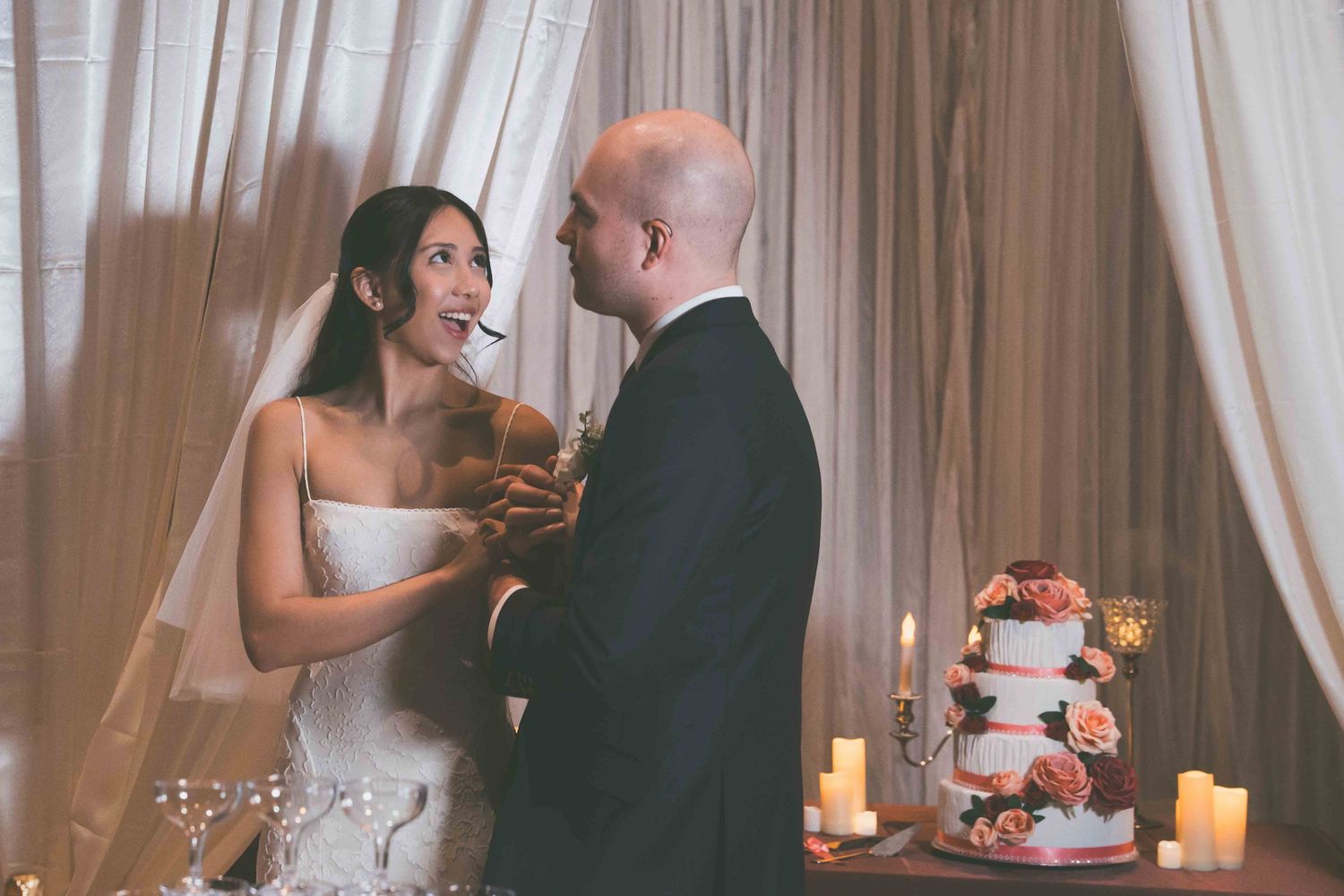 A bride and groom share a moment together near their wedding cake surrounded by glowing candles.